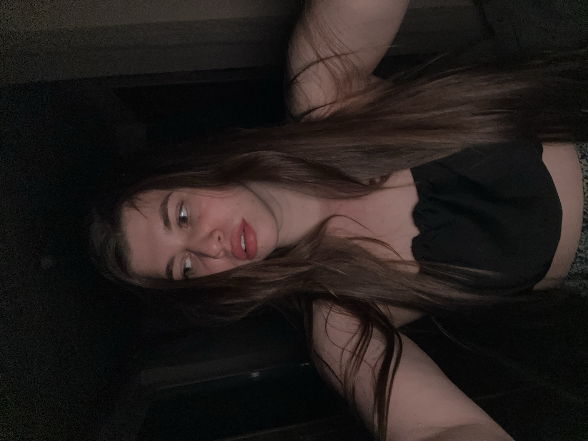 The image is a selfie of a woman with long, brown hair. She is wearing a black top. The background is dark, and the location is indistinguishable. No identifying features indicate a location in Мещёры, Russia.