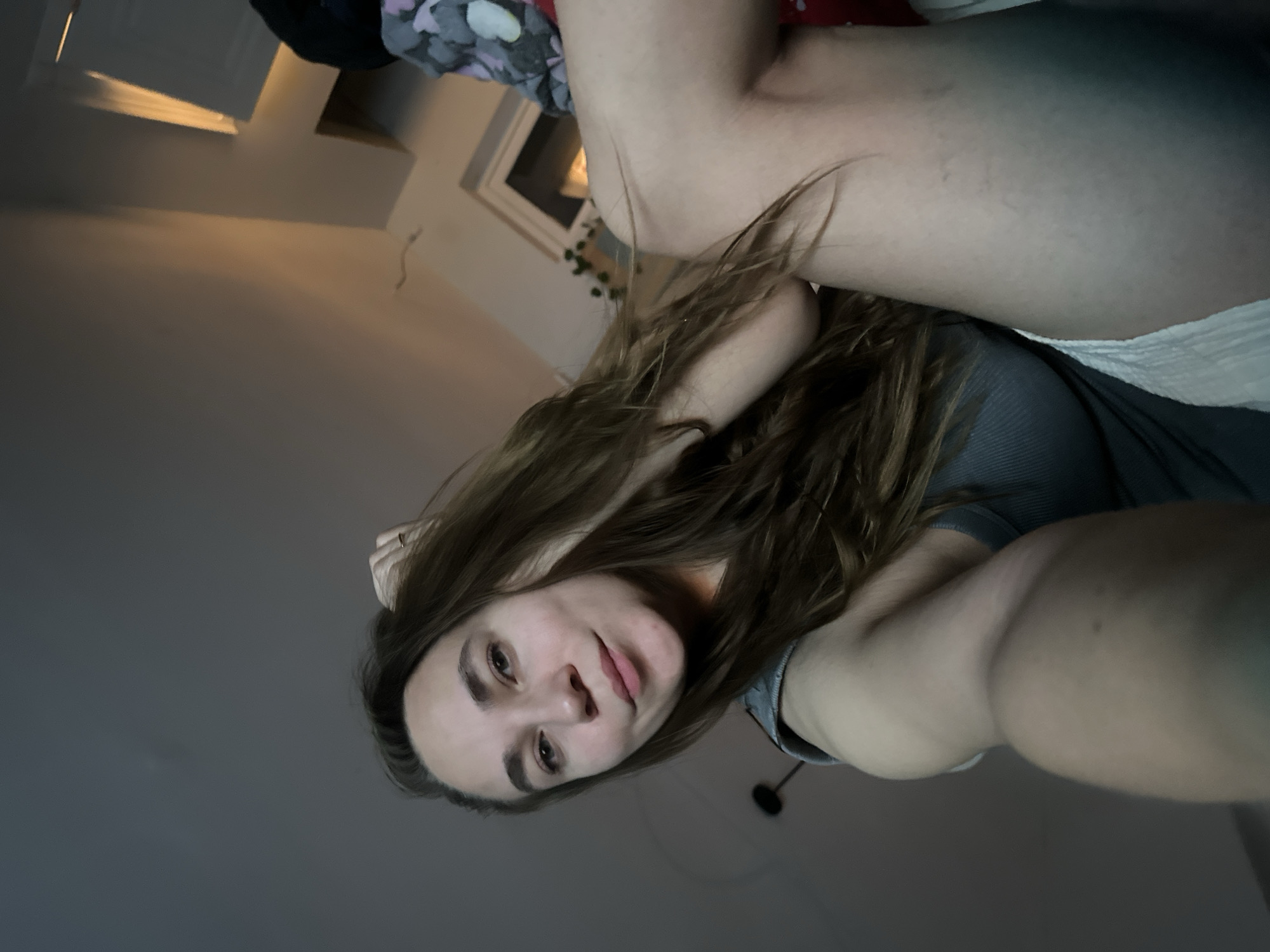 The image shows a woman with long brown hair lying down. She is wearing a gray top. The background includes a window, part of a ceiling, and what appears to be bedding or clothing. The photo's angle suggests it might have been taken from a low perspective. There is no indication in the image that it was taken in the city of Kharnavy, Russia.