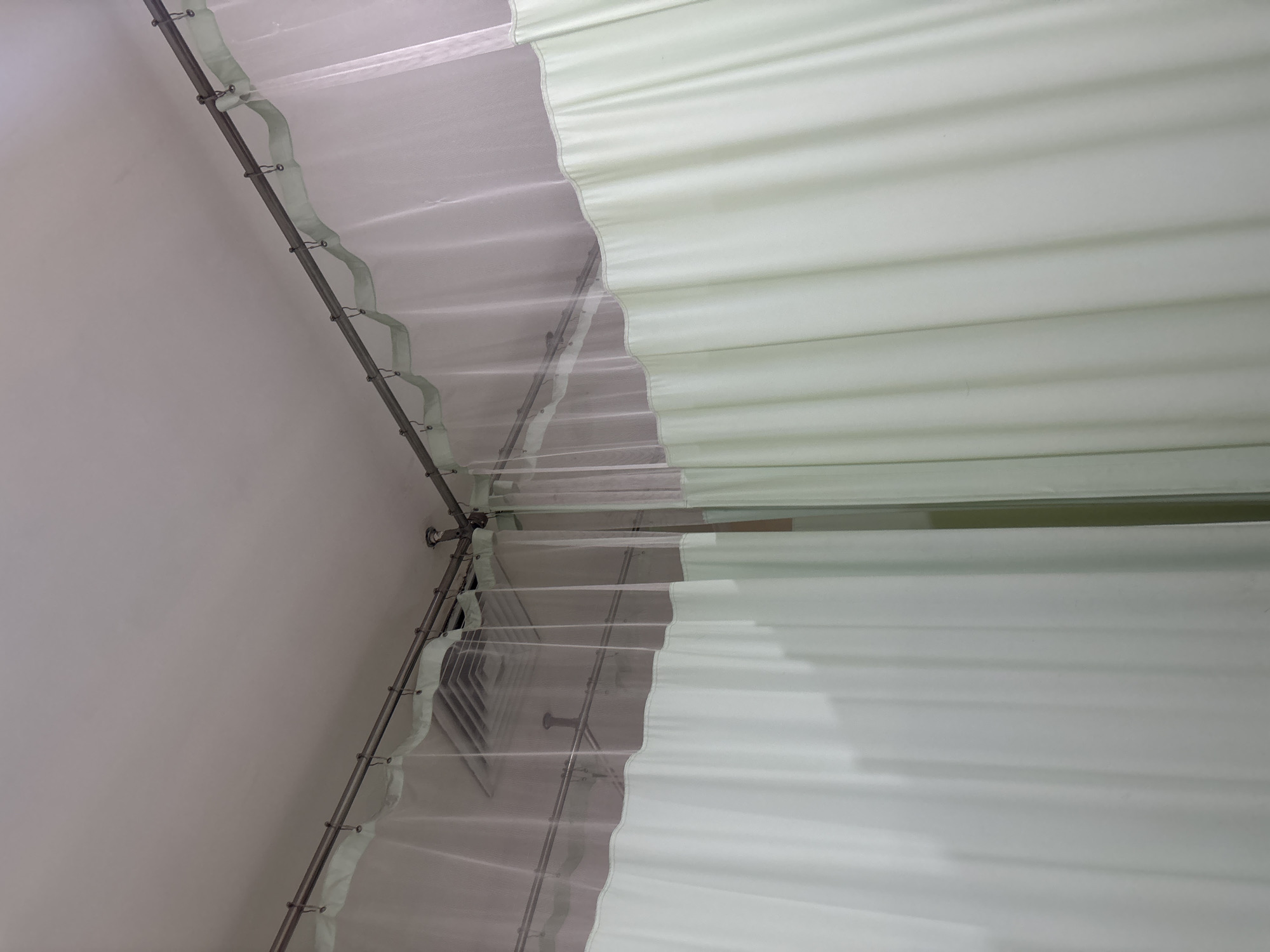 The image shows a medical curtain, typically found in a hospital room or clinic, that divides two spaces. The curtain is made of a light-colored fabric with a sheer panel at the top. It is suspended from a metal track attached to the ceiling. In the background, a ventilation grate and light fixtures are visible. The overall impression is one of a clinical or institutional setting. This type of curtain is commonly used to provide privacy for patients. The specific location of Cirebon, Indonesia, is not evident from the image itself.