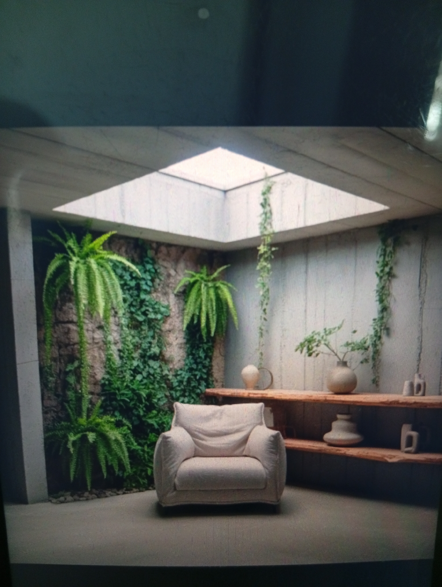 The image depicts an interior space with a square skylight providing natural light. The walls appear to be made of concrete or a similar material. On one side, a wall is covered with ferns and climbing plants, creating a natural, overgrown effect. A beige armchair sits in the center of the room. Against another wall, there's a rustic wooden shelf holding several vases and decorative objects. Vines are hanging from the ceiling. The overall scene gives the impression of a minimalist yet nature-infused interior. The location is Dutsen Alhaji, Nigeria, cannot be confirmed without additional evidence.