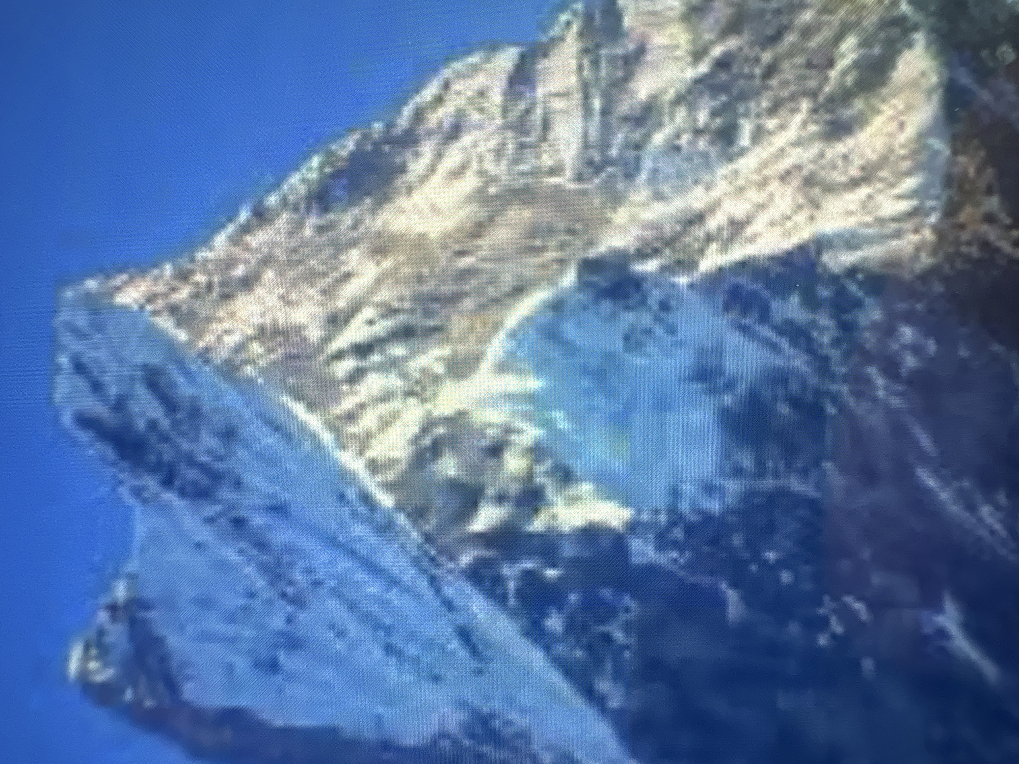 The image depicts a mountain range against a blue sky. The mountains are rocky and uneven, with variations in color from light gray to dark blue, suggesting shadows and different rock types. The texture appears rough and rugged. The scene is not identifiable within the specific location of Kukorevo, Bulgaria.