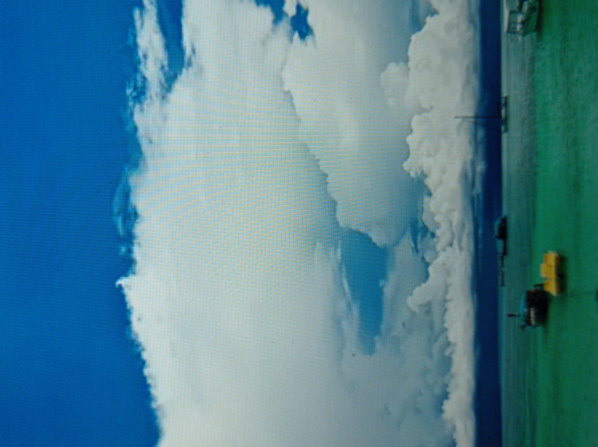 The image depicts a wide, panoramic view of a body of water under a dramatic sky filled with large, billowing white clouds. The water is a vibrant turquoise color, suggesting clear, shallow depths. Several boats are visible on the water. In the foreground, there are two smaller boats, one dark-colored and another bright yellow. Further out, a sailboat with a tall mast is silhouetted against the horizon, and to the right, a white boat with a cabin is partially visible. The sky is a deep, rich blue, with the clouds dominating the upper portion of the frame. The horizon line is clear, separating the sea from the sky, and appears to be the edge of land in the distance, a dark, misty band. There are no people visible in the image. The scene appears to be a coastal or lakeside environment, possibly a harbor or a popular boating area. It is impossible to determine the location in the city of Mukachevo, Ukraine, as the image does not contain any recognizable landmarks or geographical features specific to that city.