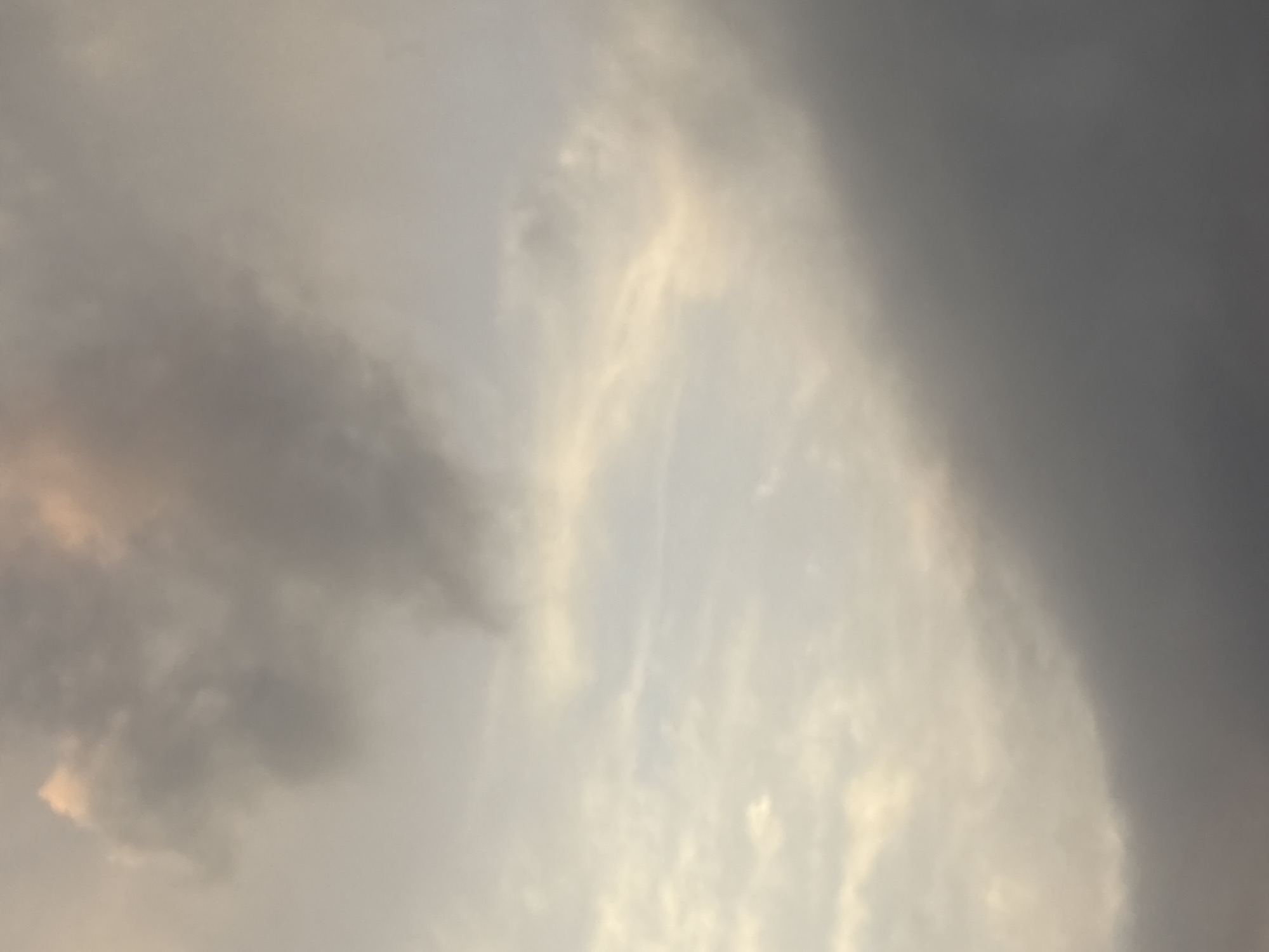 The image shows a cloudy sky, likely during sunset or sunrise, as evidenced by the soft, diffused lighting and the varied hues of the clouds. The upper portion of the sky displays lighter, perhaps wispy clouds tinged with hints of pink or peach, suggesting the sun is low on the horizon. Moving downwards, the clouds become denser and darker, with a significant portion of the lower image dominated by heavy, grey clouds, hinting at impending rain or a storm. The overall impression is a dynamic sky, transitioning from brighter, warmer tones to darker, cooler ones. The image does not contain any identifiable landmarks, people, or objects that would specifically place it within Georgiyevsk, Russia, beyond the general context of a sky.