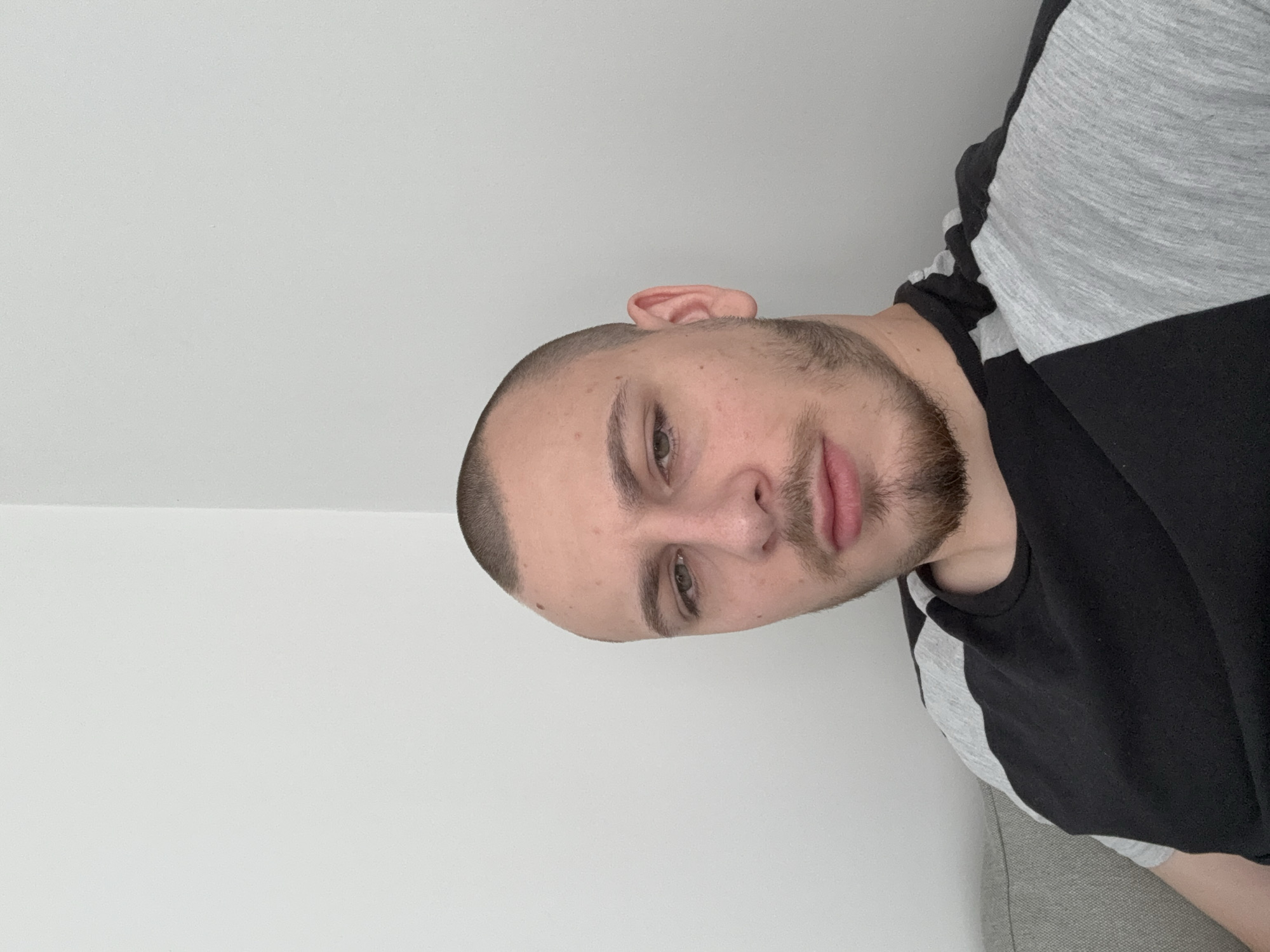 A head-and-shoulders shot of a man with short hair and a beard, wearing a black and gray shirt, set against a white wall. The location in the city of Stara Zagora, Bulgaria, is not determinable from this image.
