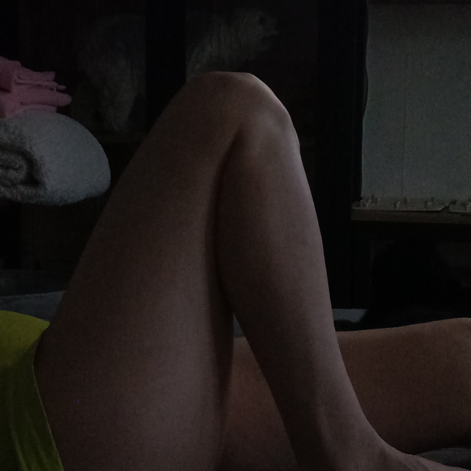 The image depicts a portion of a human body, specifically the leg of a person, bent at the knee. The person appears to be lying down. They are wearing a piece of green or yellow clothing. The background includes a dark area with objects that appear to be textiles, potentially towels or blankets. There is also a shelf or other furniture visible.
There is no information in the image to indicate that it was taken in Марковский, Russia. The provided location is not evident within the image itself.