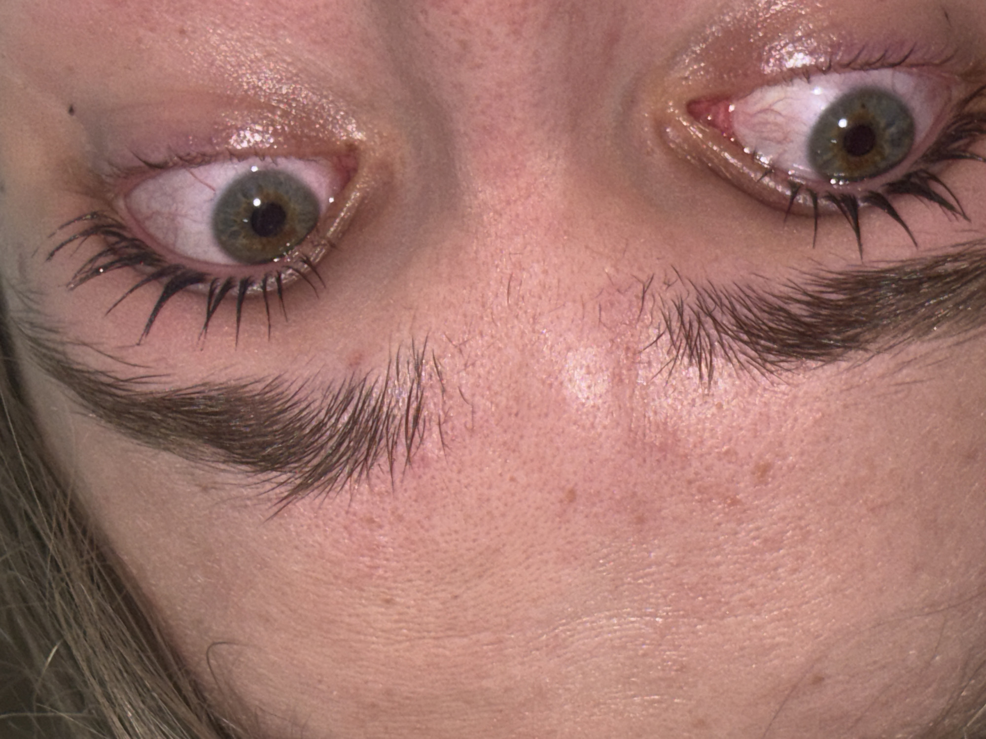A close-up of a person's face, primarily focusing on their eyes and eyebrows. The eyes are green/hazel, with visible blood vessels in the whites. Eyelashes are coated with mascara. The eyebrows are thick and untrimmed. Skin texture is visible, showing pores and minor imperfections. No information exists in the image to suggest the location is Perm, Russia, or any other specific place.