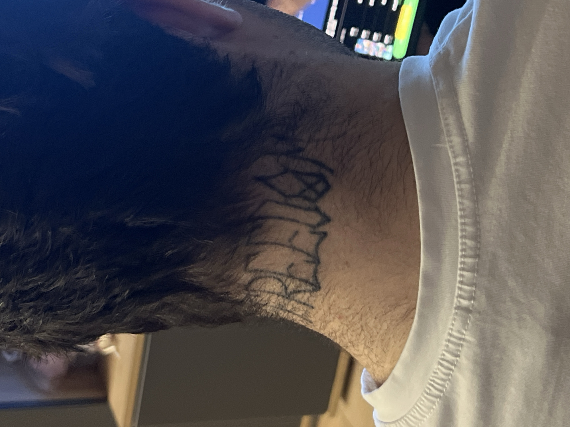 The image shows a close-up, from behind, of a person's neck with a tattoo. The tattoo appears to be in a stylized font and reads "FREUD". The person is wearing a white t-shirt. The background is blurred, but suggests an indoor setting with a wooden surface and a screen displaying colorful graphics. The location in the city of Moscow, Russia cannot be determined from the provided image.