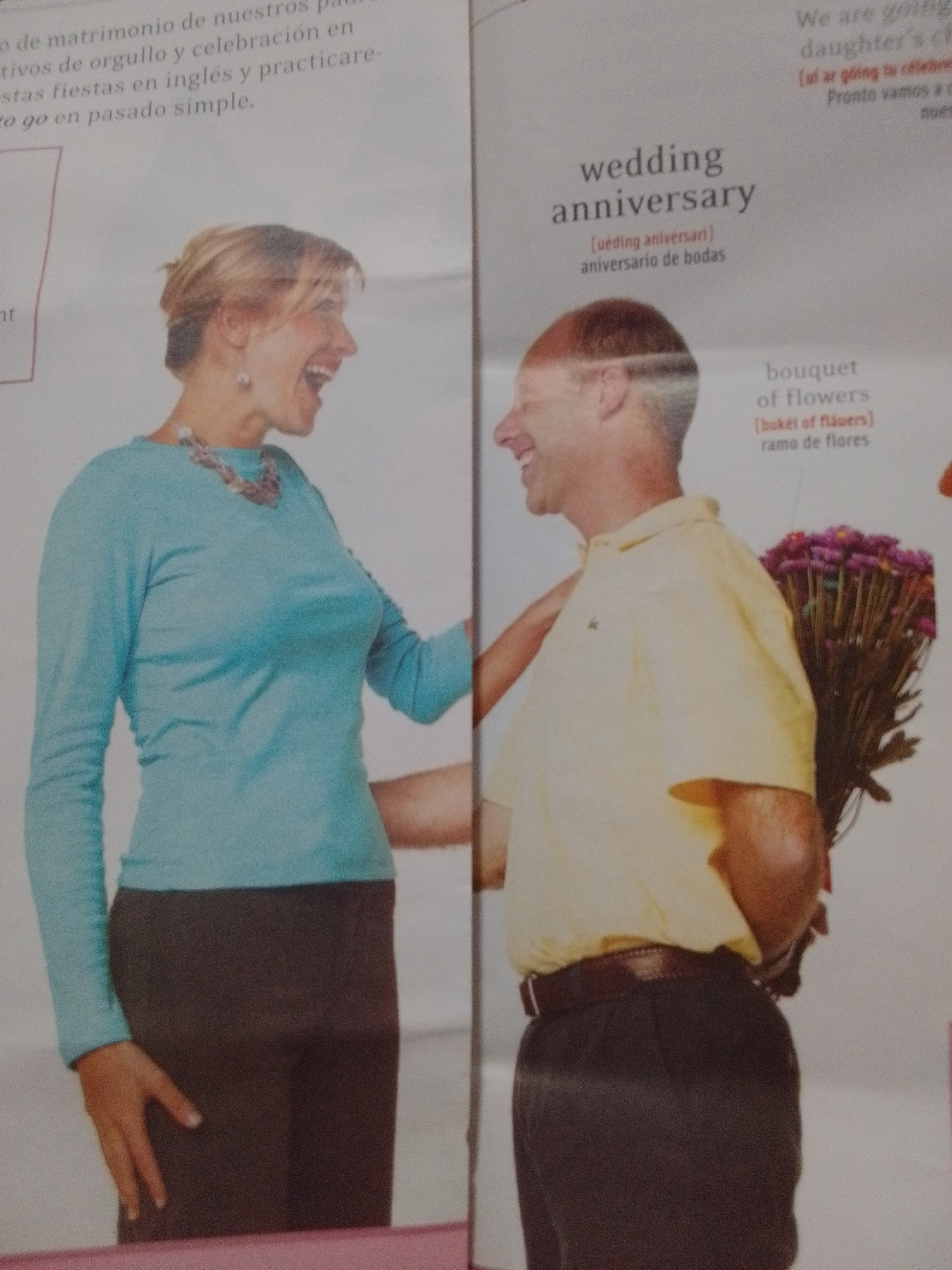 The image shows two individuals, a woman and a man, in what appears to be a magazine spread. The woman, on the left, is wearing a light blue long-sleeved shirt and a dark skirt, with a statement necklace. She has blonde hair and is looking to her right with her mouth open, as if laughing or speaking. The man, on the right, is wearing a yellow polo shirt and dark pants. He is holding a large bouquet of purple flowers behind his back, suggesting he is about to present them to the woman. The text in the background includes titles like "wedding anniversary" and definitions in English and Spanish, indicating the context of a celebration or gift-giving occasion. The specific location in the city of La Tagua, Venezuela, is not discernible from the provided image.