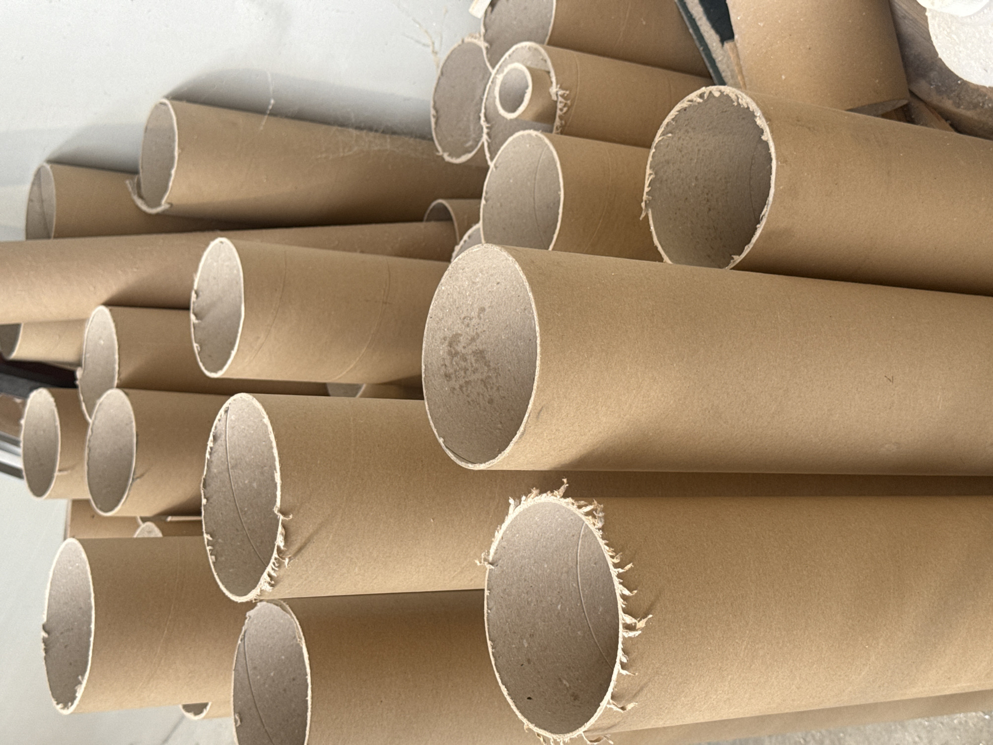 The image shows a collection of cardboard tubes, likely used as cores for paper or other rolled materials. They are standing upright, in various sizes and heights, and are arranged in a dense grouping against a plain, light-colored wall. Some of the tubes are partially visible, suggesting they are stored in a warehouse or workshop. The lighting is even, and there are no people or other discernible objects in the scene. The location is not specified in the image itself, and thus, its presence in the city of Fontevivo, Italy cannot be confirmed.