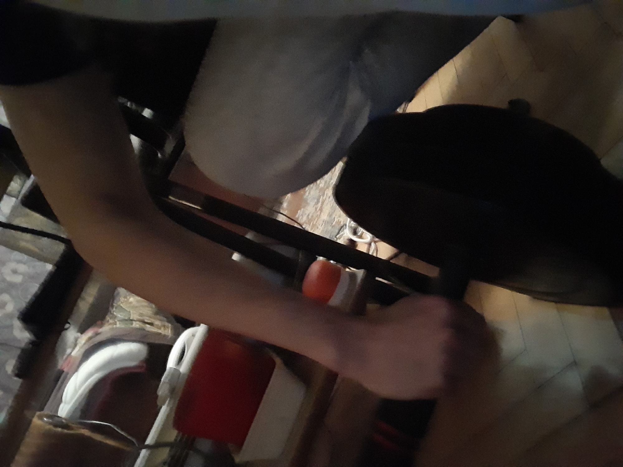 A person's arm is visible from the shoulder down, the hand is obscured. A black hat is on top of cardboard. A white chair and a red box are also present. The location and setting cannot be determined.