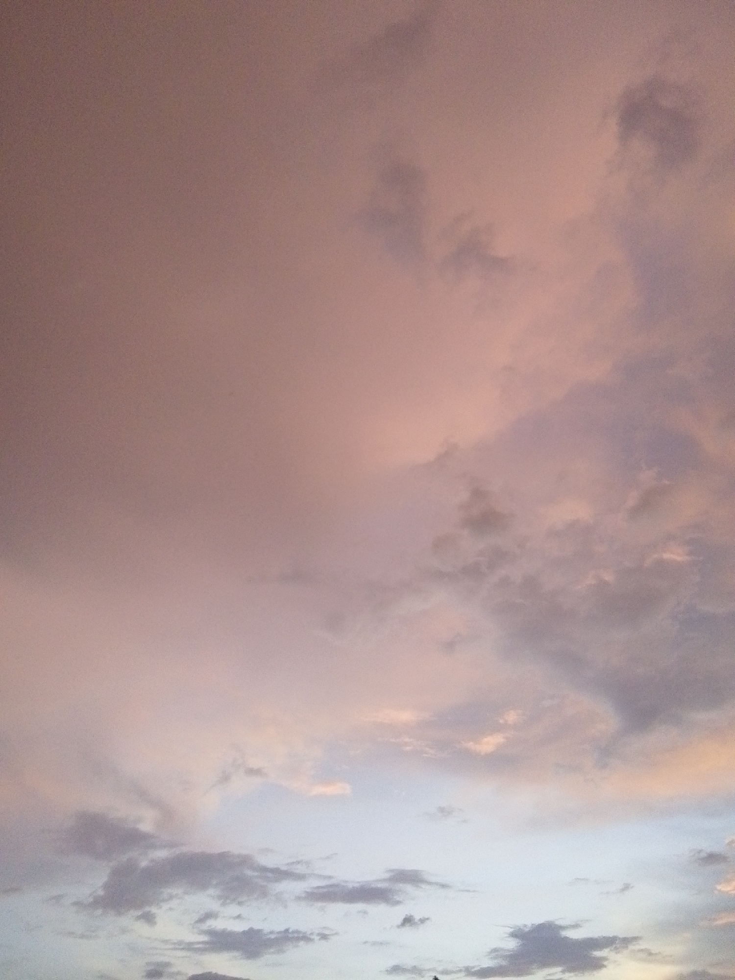 The image depicts a sky filled with clouds, exhibiting a gradient of colors from soft pinks and oranges at the top to lighter blues and grays towards the bottom. The clouds are varied in texture and density, with some appearing wispy and others more substantial. The lighting suggests it could be either sunrise or sunset. There are no visible people, subjects, objects, or actions within the frame. The environment is entirely the sky. The location is specified as Serti, Nigeria.