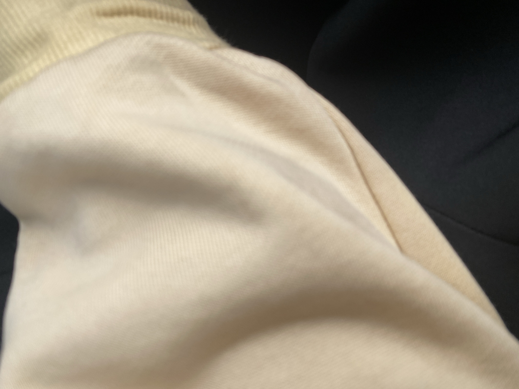 This media file is a close-up, abstract shot of a light-colored, textured fabric, possibly a garment like a sweatshirt or hoodie. The fabric has a ribbed texture, particularly visible towards the top left of the frame, and appears to be a soft material like cotton or fleece. There are subtle folds and wrinkles in the fabric, suggesting it is either being worn or is in a relaxed state. The background is a dark, out-of-focus area, which could be another piece of clothing or a dark surface. The lighting is soft, highlighting the texture and contours of the fabric. There is no discernible activity or event taking place; the image focuses solely on the tactile qualities of the material. No text or specific location cues are visible within the frame, other than the provided location context of Jalingo, Nigeria. The overall impression is one of comfort and texture.
