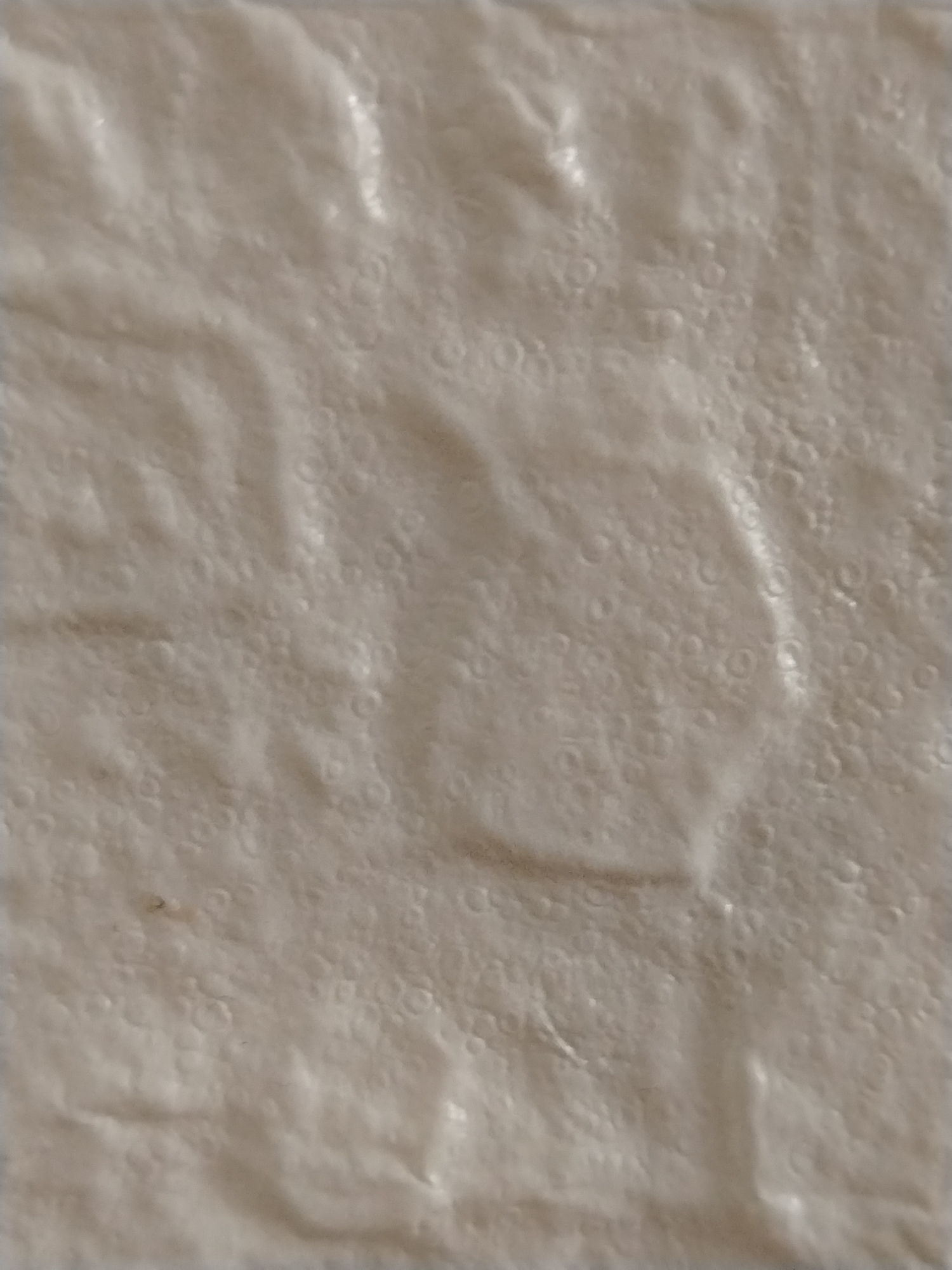 The image displays a close-up, abstract view of a crumpled, light-colored material, possibly paper or fabric, with a textured surface featuring numerous small, circular indentations and larger, softer folds. The lighting creates subtle highlights and shadows, emphasizing the material's unevenness. There are no identifiable objects, people, or contextual elements that would suggest a specific location, including the city of Stavropol, Russia. The image is purely textural.