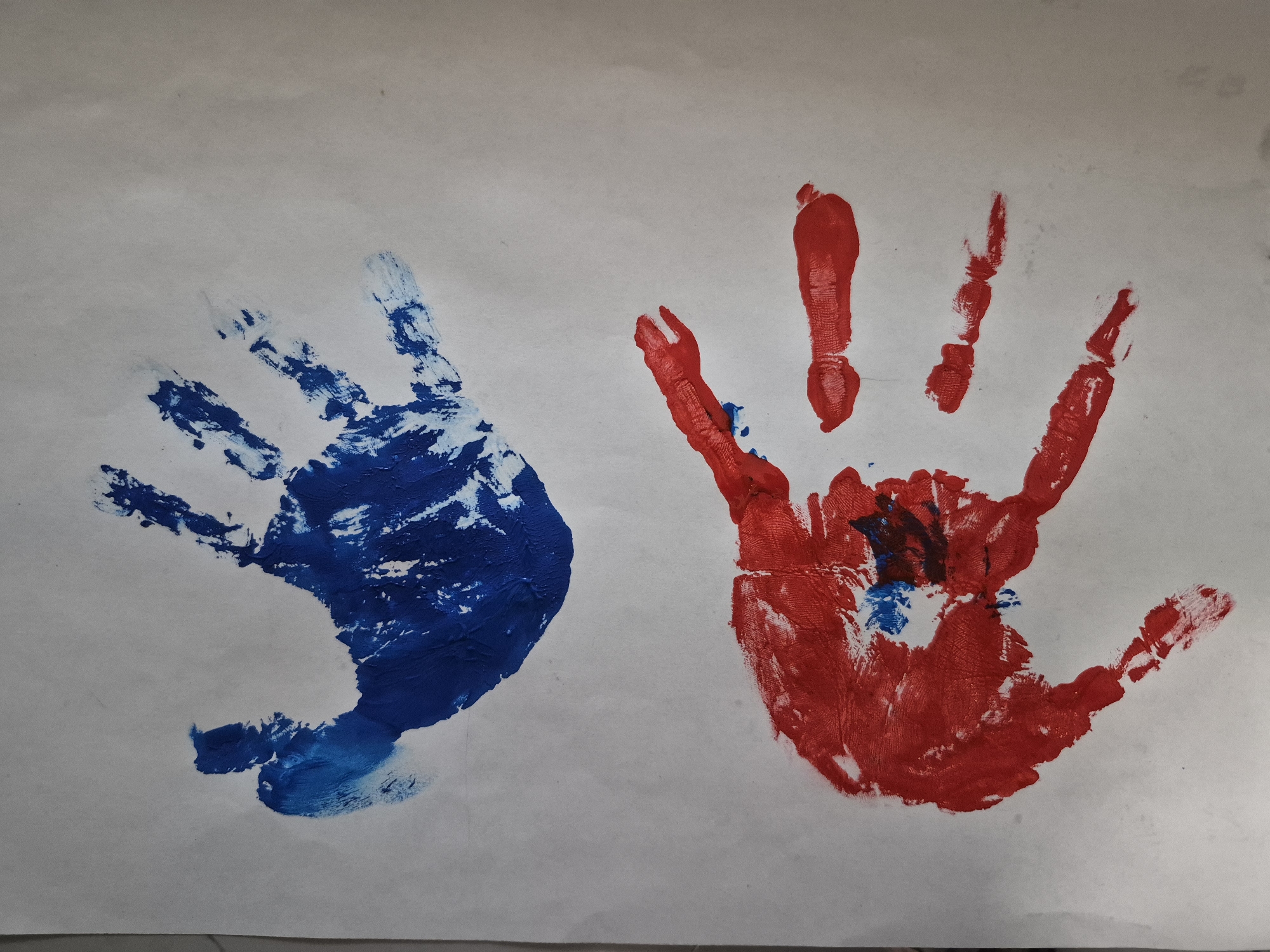 The image shows two handprints on a white surface, presumably paper. The handprint on the left is blue, and the handprint on the right is red with some blue and dark smudges in the center. The image contains no information to determine the location in the city of Tobolsk, Russia, or any other specific details.