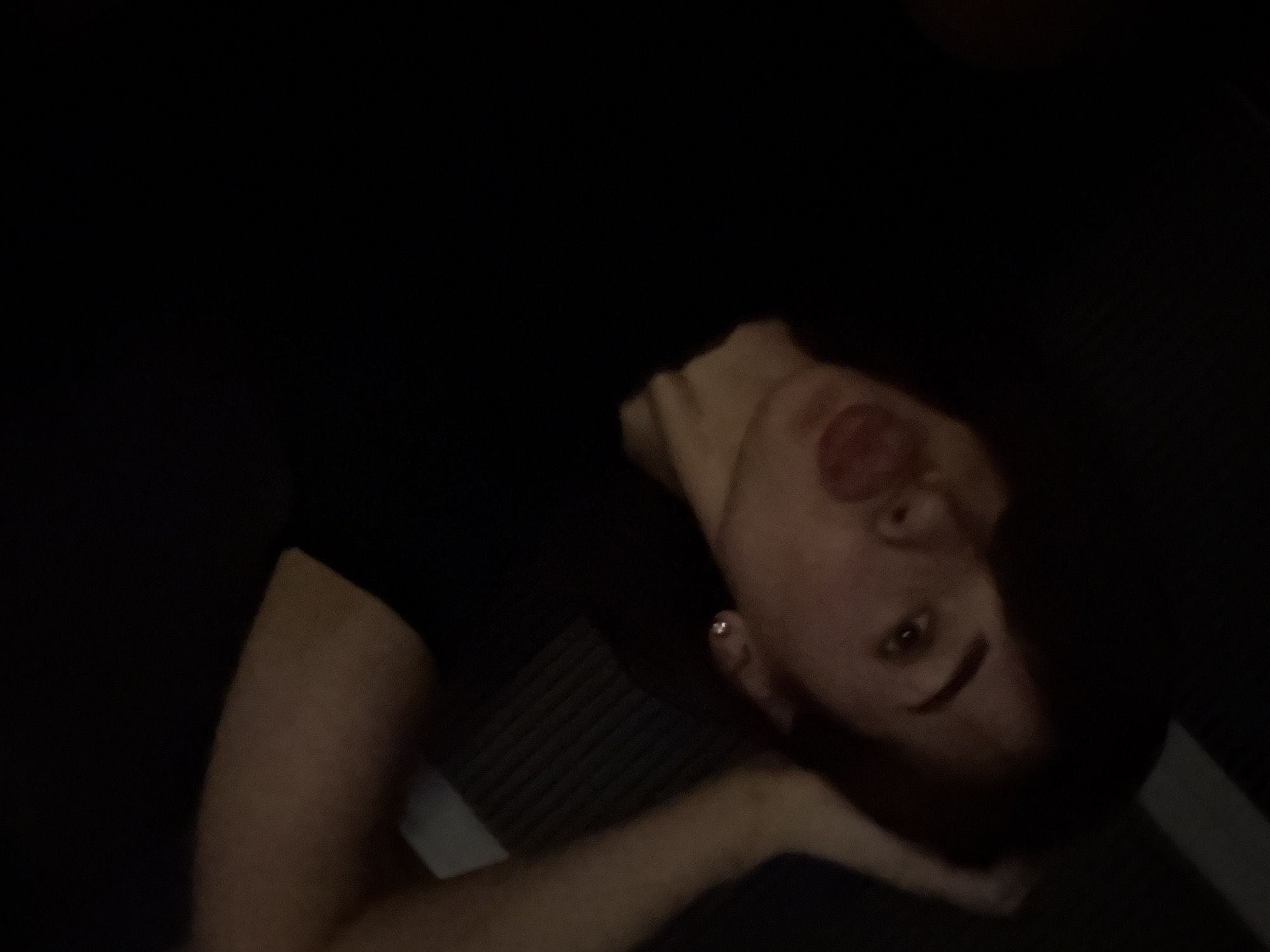 A dimly lit close-up shot of a person lying on their side. The person's face is visible, with features including lips, nose, and eyes. Part of an arm is visible resting near the head. The background is dark and unclear. The location of Лобаново, Russia is not apparent from the image.