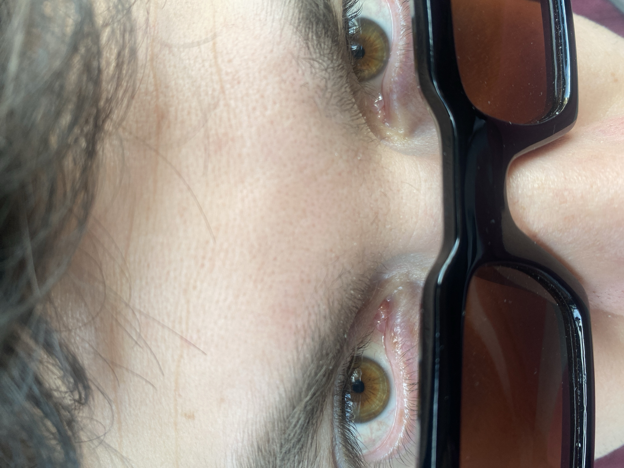 The image is a close-up of a person's face, rotated counter-clockwise. The person has fair skin, brown hair, and brown eyes. Sunglasses are visible on the right side of the image. No information is available regarding the location in Varna, Bulgaria, or any further details about the environment.