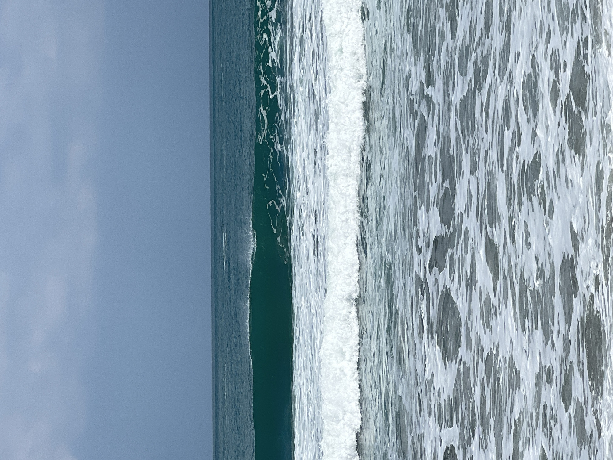 The image shows a wide shot of the ocean with waves breaking. The sky is overcast and a pale blue. The ocean is a deep teal color in the distance, transitioning to lighter blues and whites as the waves approach the shore. There are multiple sets of waves visible, with the closest ones forming white foam. The overall impression is of a calm, yet dynamic, ocean scene. The image does not depict any specific location in Kuta, Indonesia, nor does it contain any people or objects.