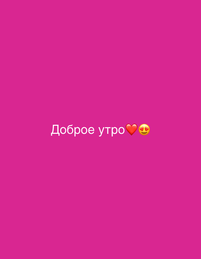 The image is a close-up, eye-level, medium shot of a pink background with white text that reads "Доброе утро" (Good morning) in Russian, followed by a red heart emoji and a yellow smiley face emoji with hearts for eyes. The text and emojis are centered horizontally and located towards the bottom of the frame. The lighting is even and bright, suggesting an artificial light source or a well-lit environment. There is no visible environment or context beyond the colored background and the text.