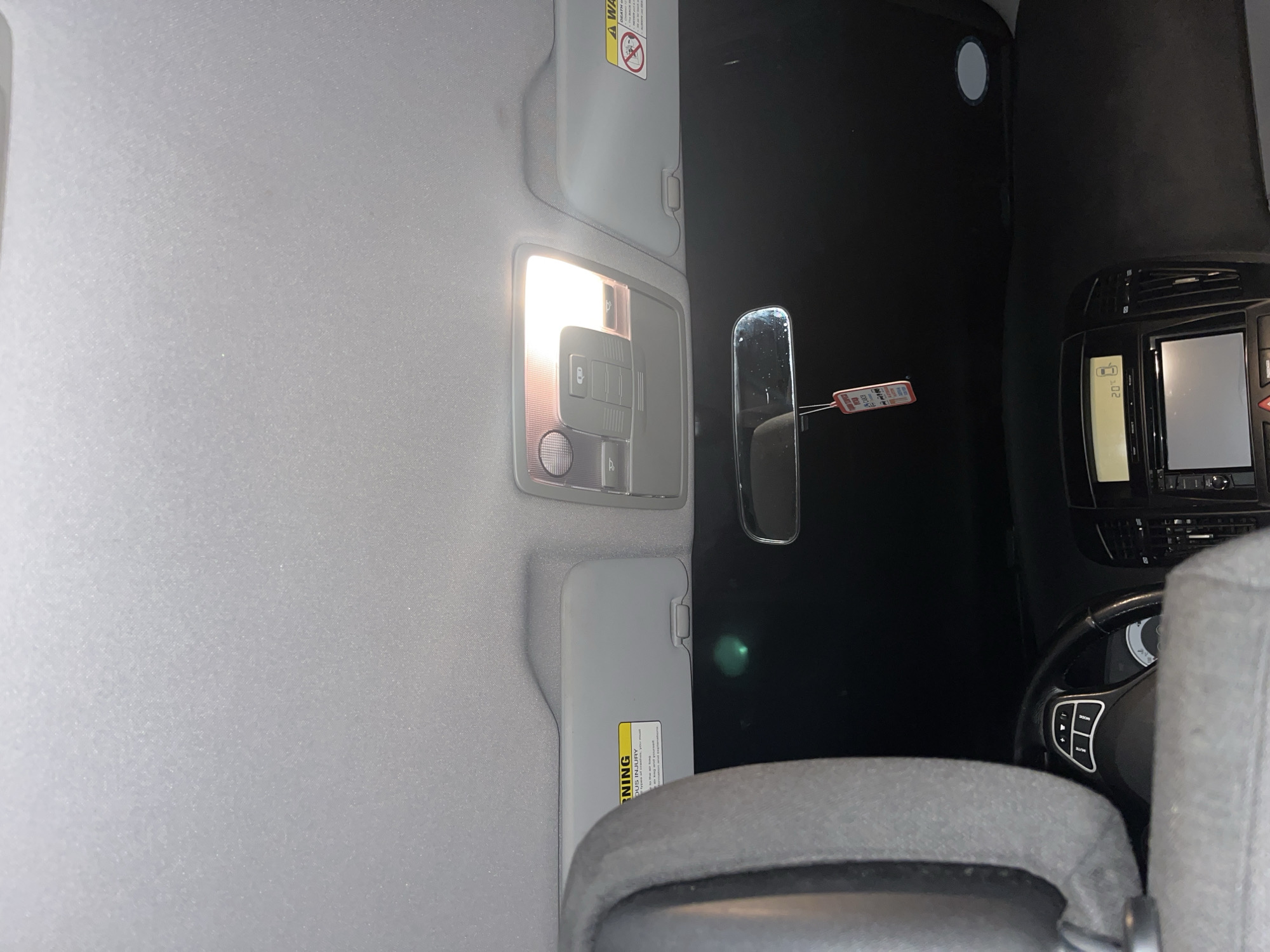 Interior view of a car cabin with a gray dashboard, seat, and ceiling. A rearview mirror hangs centrally. The overhead light is on. A steering wheel with control buttons is visible. The car's infotainment system displays temperature and other information. There is no visible indication of the location being Marulevo, Bulgaria, nor are any people visible.