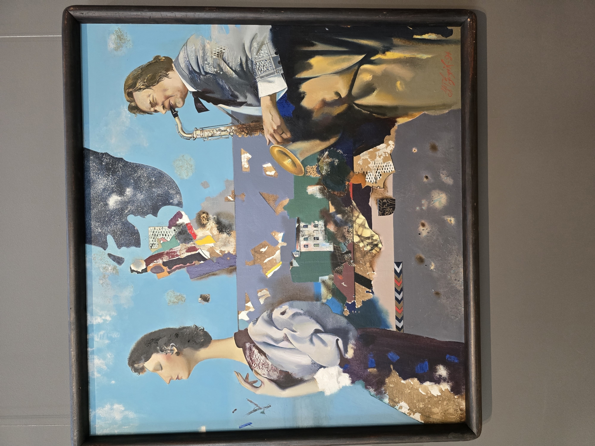 This is a painting depicting two figures against a surreal, fragmented background, framed in dark wood. On the left, a woman with dark hair is shown in profile, her eyes closed, wearing a light-colored jacket with a white ruffled trim. Her left hand is raised, touching her neck. To the right, a man with light brown hair plays a saxophone. He wears a light-colored suit with a dark bowtie. The background is a collage of abstract shapes, architectural elements resembling buildings, and what appear to be torn pieces of paper or fabric, set against a bright blue sky with scattered clouds. The painting is signed in red script in the lower right corner, "A. Gribok, 94." The painting is displayed on a gray wall, likely in a museum or gallery, as indicated by a thin wire suspension hook visible in the upper right corner. The exhibition context suggests it might be displayed in the National Art Museum of the Republic of Belarus in Minsk.
