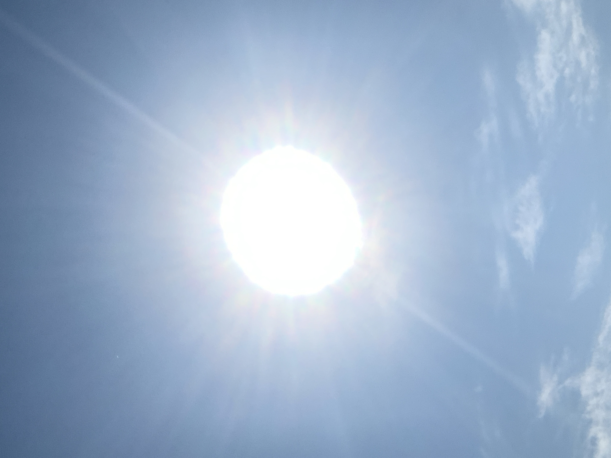 The image is a photograph of a bright sun in a clear blue sky, with some wispy clouds at the bottom. The sun is very luminous, with rays of light emanating outwards. There are no people, objects, or actions depicted. The scene appears to be an outdoor environment, likely during the daytime. The reference to Kolomyia, Ukraine, is external information and not directly derivable from the visual content of the image itself.