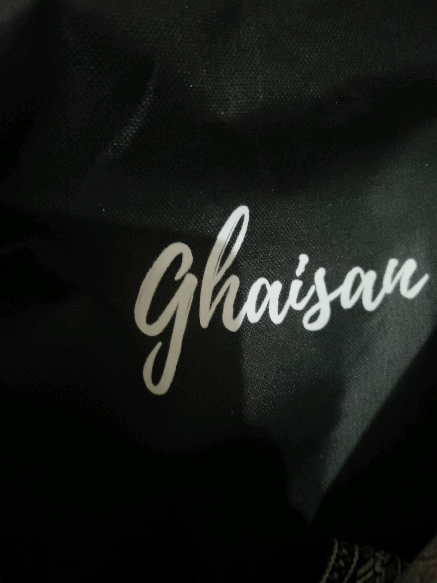 The image displays the word "Ghaisan" written in white cursive script on a black, textured surface, possibly fabric. The lettering is the primary subject of the image. There is no discernible location in the city of Serang, Indonesia, visible in this image. The lighting creates shadows and highlights on the surface, emphasizing the texture.