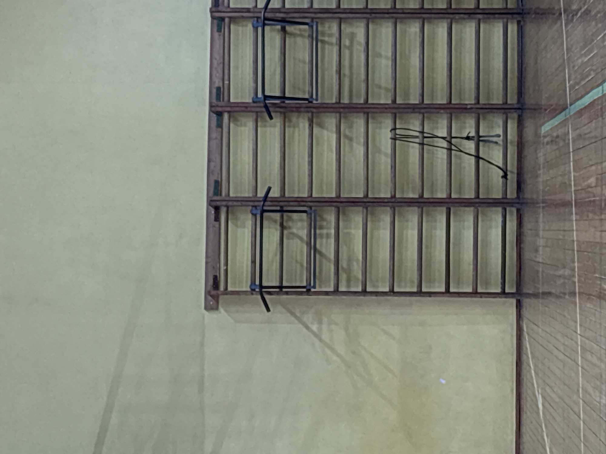 The image shows a climbing frame with metal bars attached to a wall. The wall is yellow-green, and the frame is brown. There are some metal objects hanging on the bars. The floor beside the wall is made of wood planks. The photograph does not contain any information about Izhevsk, Russia.