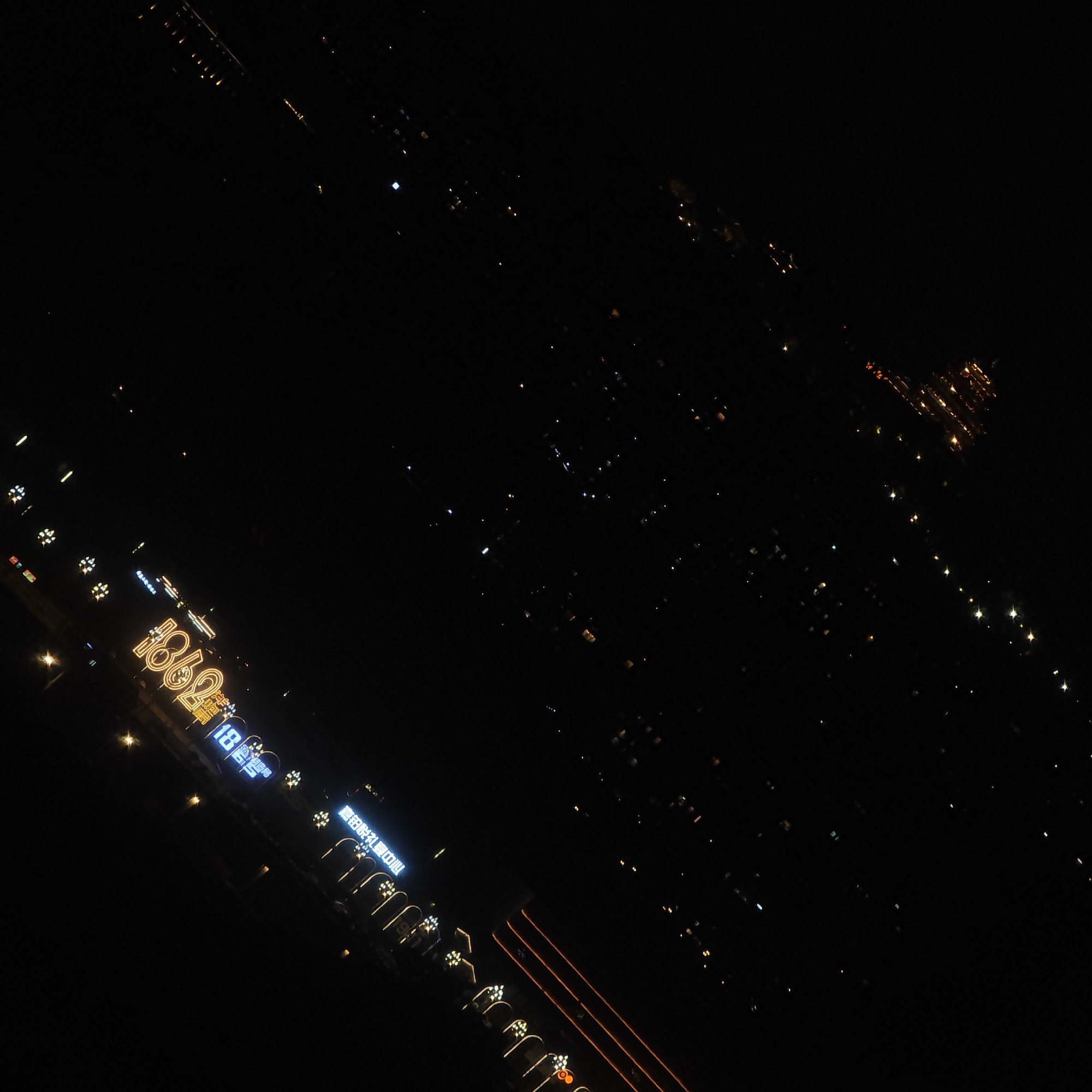 The image depicts a nighttime view, likely from an elevated position, over Yuzhong District, Chongqing, China. The district is characterized by a multitude of lights, which indicate urban development. Lit signs, including "1862" and "喜田婚礼宴会中心", are visible. The landscape seems to incorporate a mix of buildings and infrastructure.