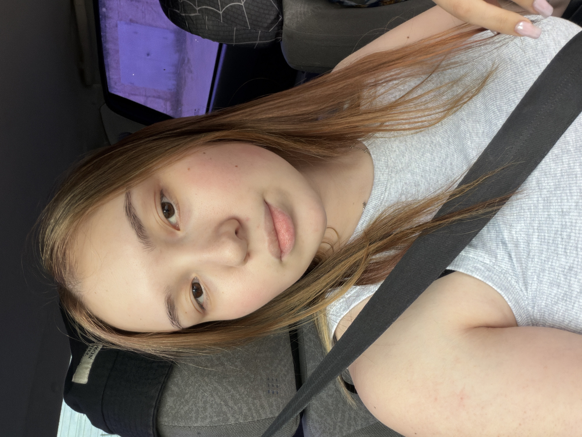 A young woman is in a car, secured by a seatbelt. She is wearing a grey t-shirt. The location is Chaikovsky, Russia.