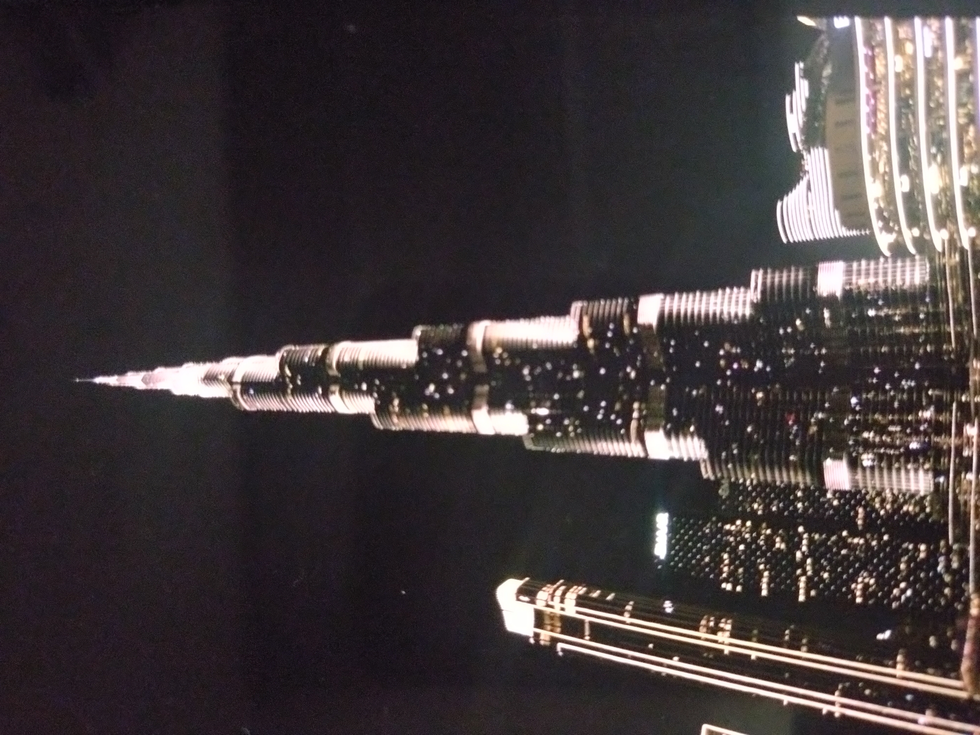 The image shows a nighttime view of the Burj Khalifa skyscraper in Dubai. The tower is brightly lit and dominates the dark background, with other buildings visible in the lower portion of the frame. It is not in Stara Zagora, Bulgaria.
