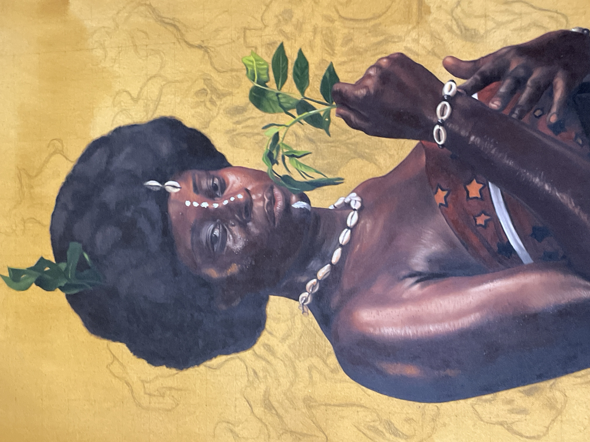 The image depicts a painting of a person with dark skin and hair, adorned with cowrie shells on their forehead and around their neck. A green branch is positioned near their face, and the person is holding another branch in their hand. They are wearing a bracelet made of cowrie shells. The background is a golden color. There is no information in the image that provides details about the city of Ado, Nigeria.
