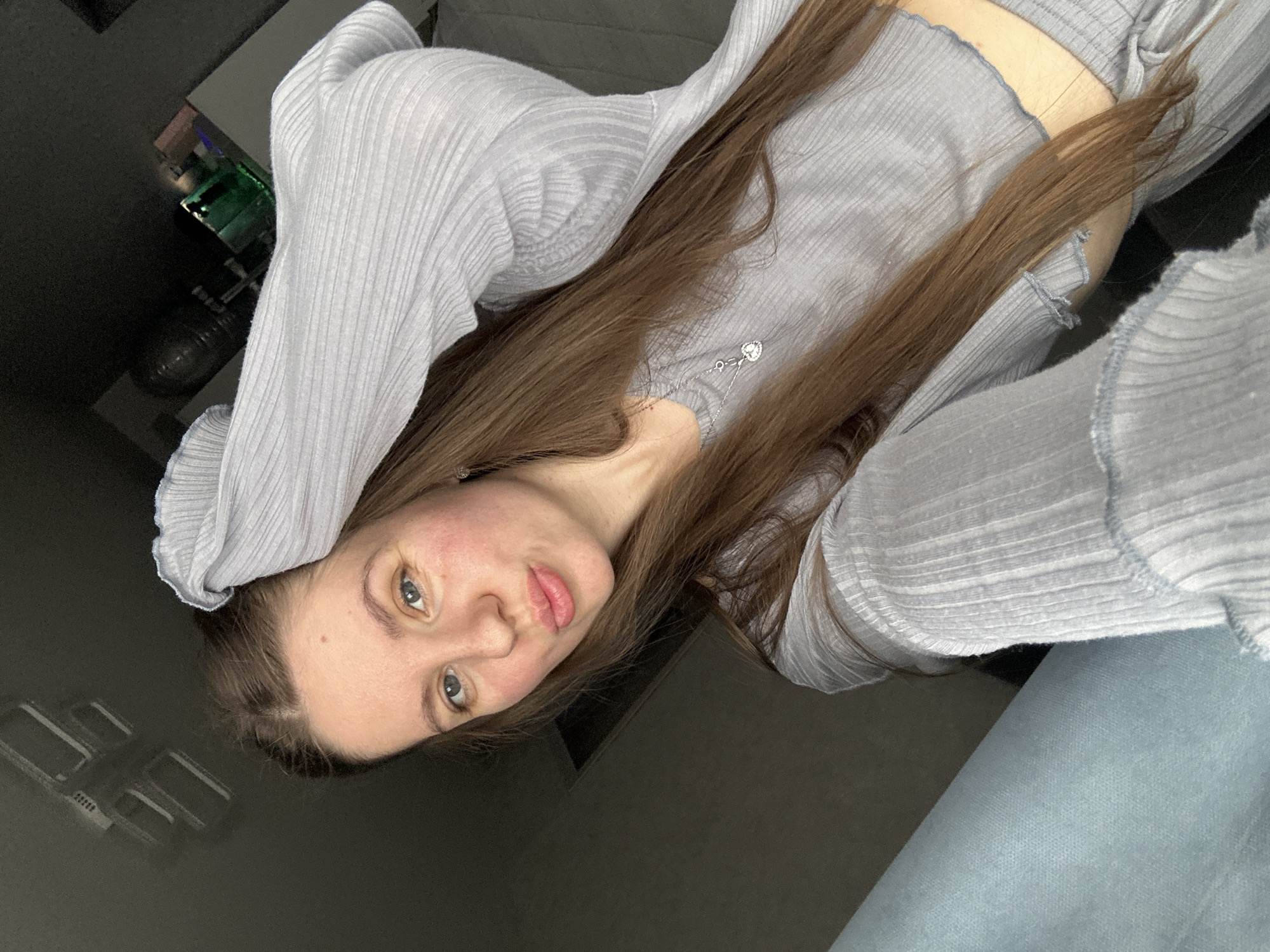 A young woman with long brown hair is lying down, facing the camera. She is wearing a light blue ribbed top and bottoms. Her head is tilted slightly. The background is dark and indistinct. It is not possible to confirm any location.
