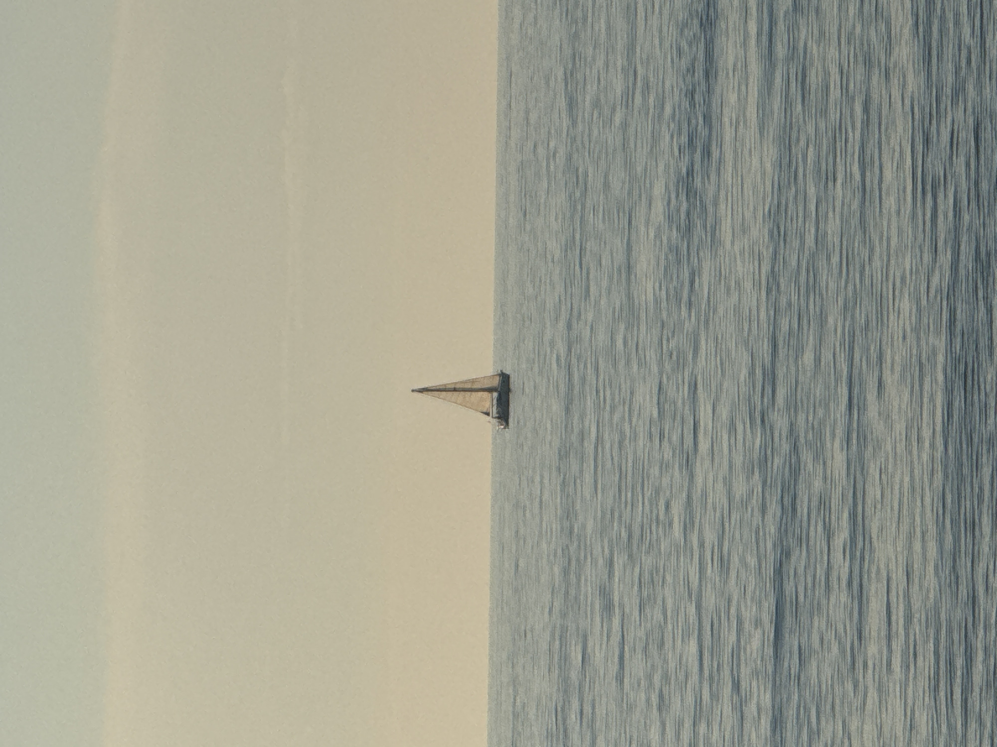 The image depicts a sailboat sailing on the Black Sea off the coast of Batumi, Georgia. The composition is divided vertically with the sea on the right and a pale sky on the left. The sailboat is positioned near the center of the frame, with its sails visible against the lighter background. The sea has a textured surface, suggesting wind or slight waves.