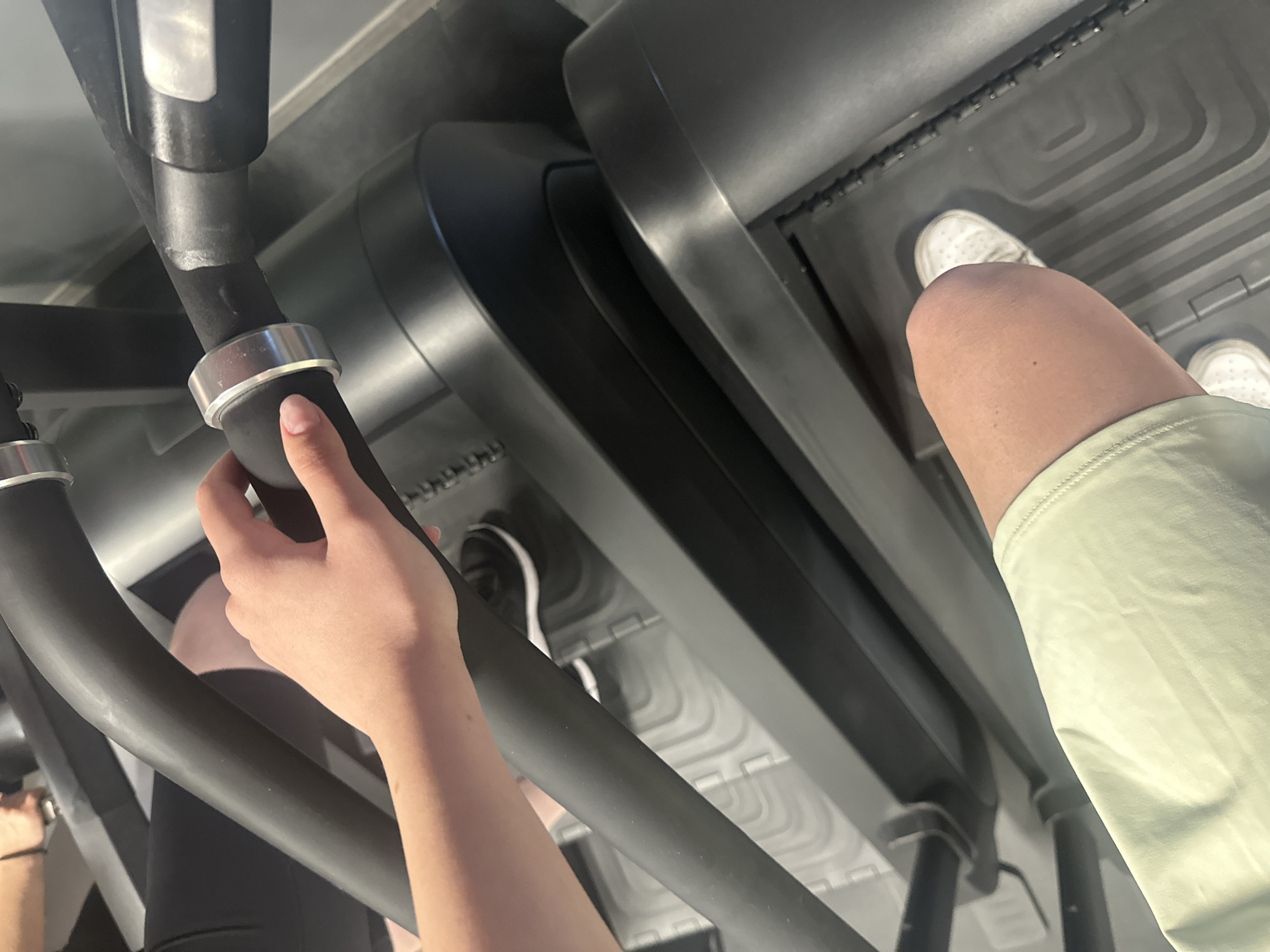 A first-person perspective image shows an individual on a treadmill indoors. The person is holding onto the treadmill's handrail with their left hand. Part of their right leg and foot, clad in a white athletic shoe, is visible on the treadmill belt. The environment is a gym, with a treadmill. The location is not discernible from the image. Yerevan, Armenia cannot be determined.