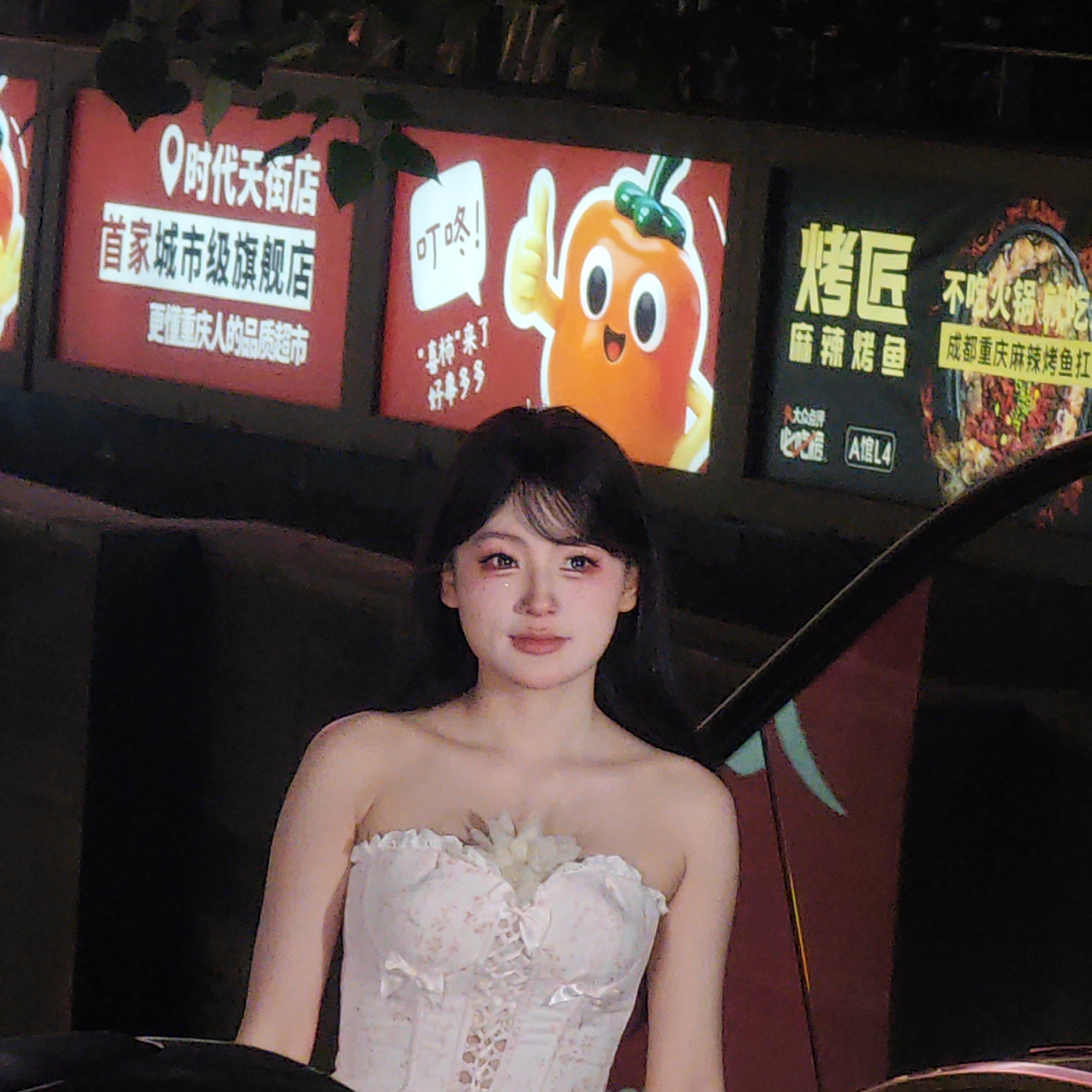 The image shows a young woman in a white, floral-patterned corset, standing in front of a wall with several illuminated advertising signs. The signs feature Chinese characters, images of a cartoon pepper character, and various food advertisements. The woman has dark hair, pale skin, and appears to be wearing makeup. The setting suggests an urban area in China, specifically Yuzhong District based on the signs.
