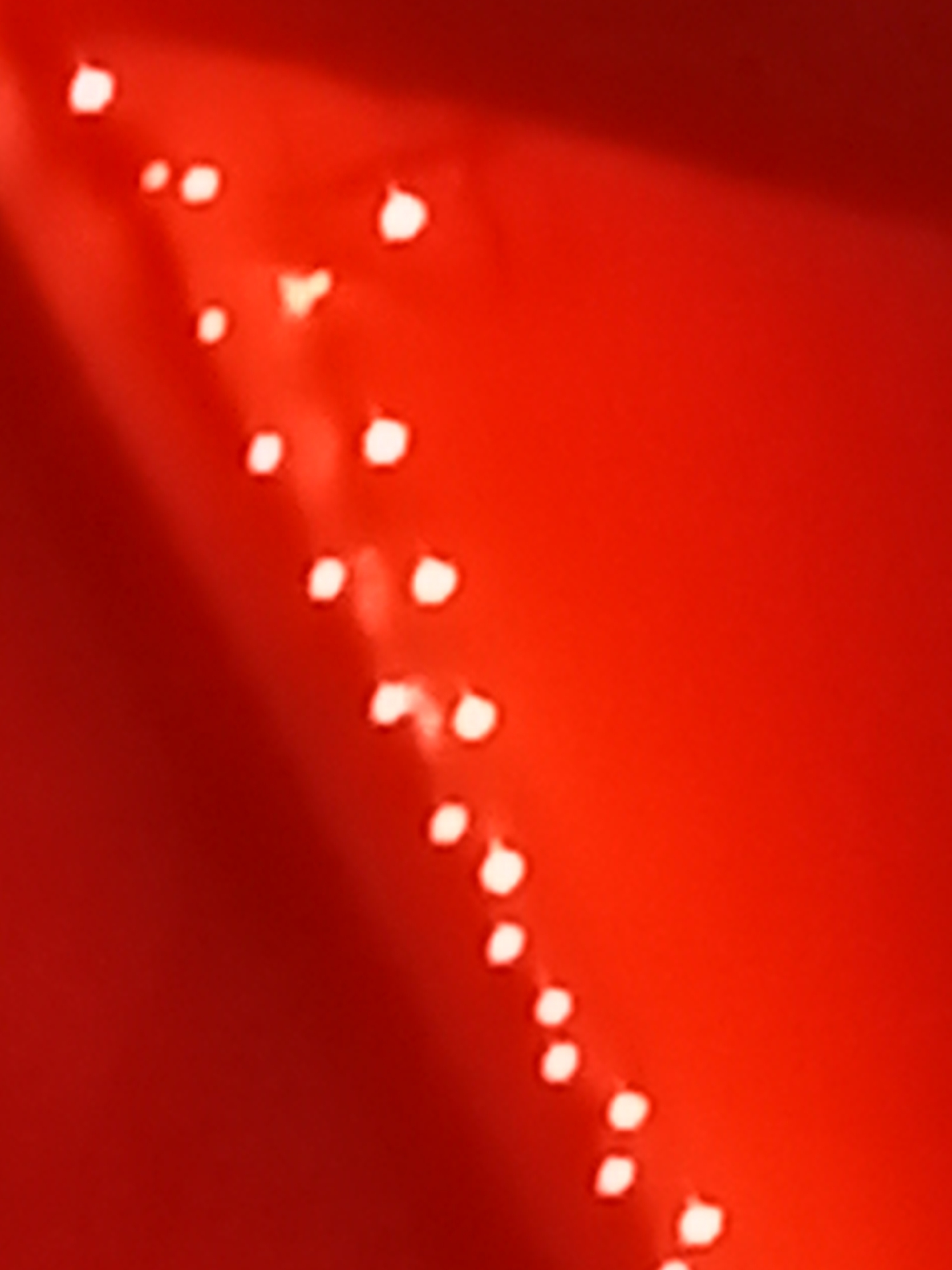 The image shows a blurred view of red string lights against a red background. The lights are small and circular, and they appear to be arranged in a diagonal line. There is a bright light source in the upper left corner of the image, which is causing a glare on the red background. The image is out of focus, and it is difficult to discern any specific details. There is no information provided about the location in the city of Kuyantaevo, Russia.