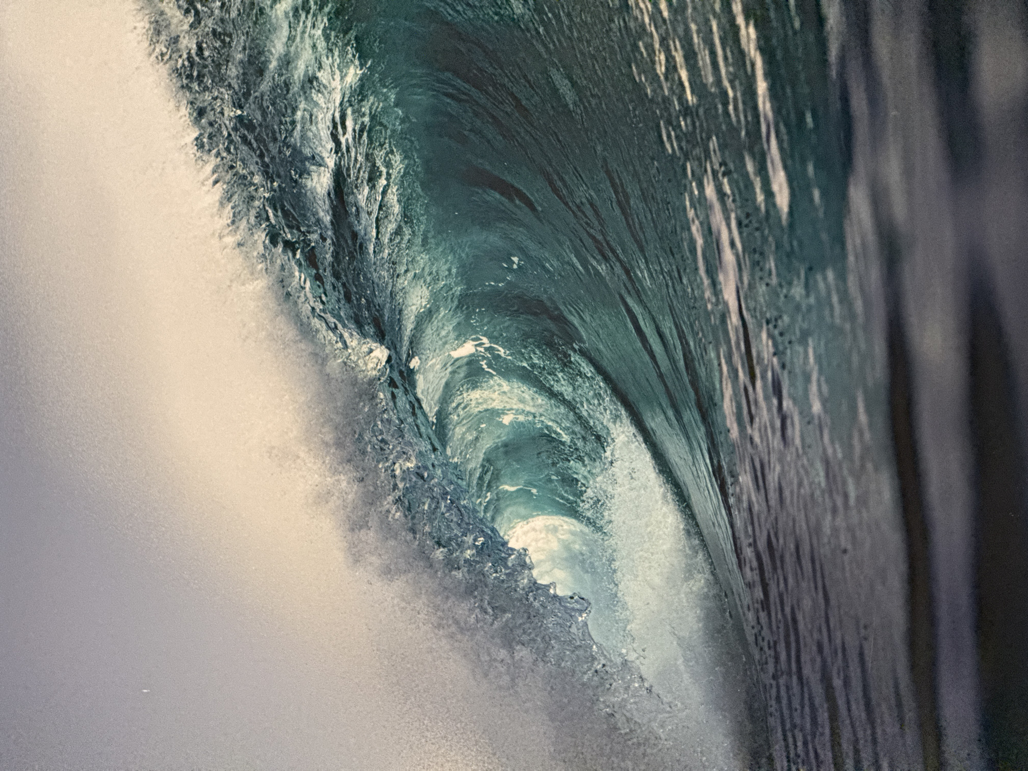 The image shows the inside of a breaking wave, likely at Kuta Beach, Indonesia. The wave is a swirling mass of white foam and turquoise water, with the smooth, unbroken part of the wave on the right. Light is visible through the curl of the wave, creating a bright spot within the darker water.