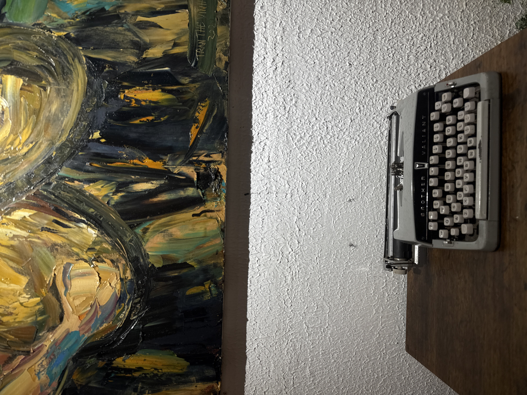 This media file shows a close-up view of a textured white wall with a vintage Brother Valiant typewriter mounted on a wooden shelf. To the left of the wall, a portion of an abstract oil painting is visible. The painting features thick, impasto brushstrokes in dark blues, yellows, and blacks, with some circular elements in lighter yellows. There is some visible text on the painting that reads "TRAN THE VINH" and "2024". The typewriter is grey and white with black lettering on the keys. The scene appears to be indoors, with artificial lighting casting shadows. The overall impression is one of a creatively decorated space, possibly an artist's studio or a personal collection display. The specific location is given as Da Lat, Vietnam.