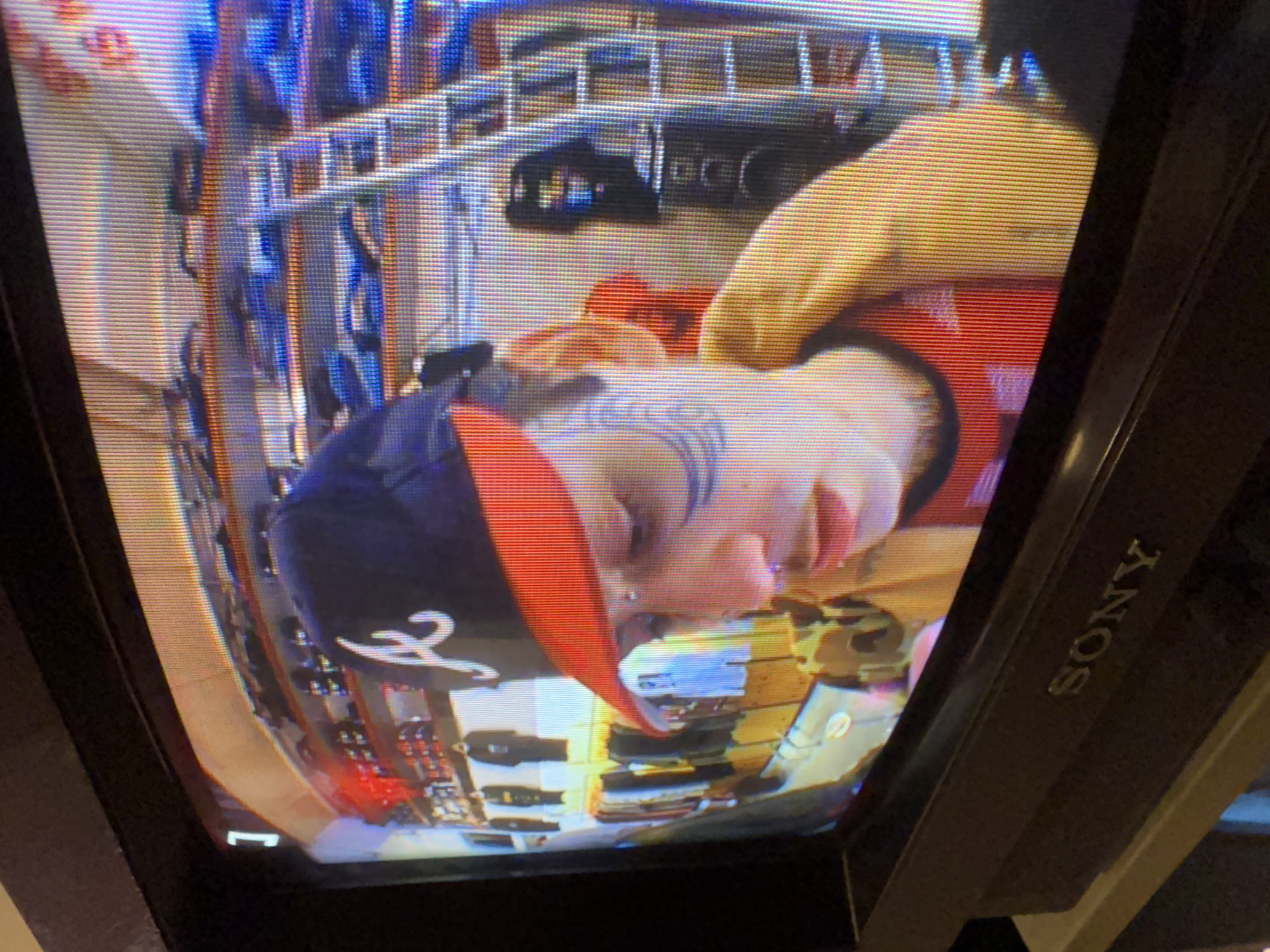 The image displays a person with tattoos wearing a baseball cap with an Atlanta Braves logo, captured on a Sony television screen. The person's face is visible, and they appear to be inside a shopping cart. The background shows a retail environment with various items displayed on shelves or racks. The scene is likely from a store, and the details suggest it might be a candid shot from the television, although there is no definitive evidence of its location in Buenos Aires, Argentina.