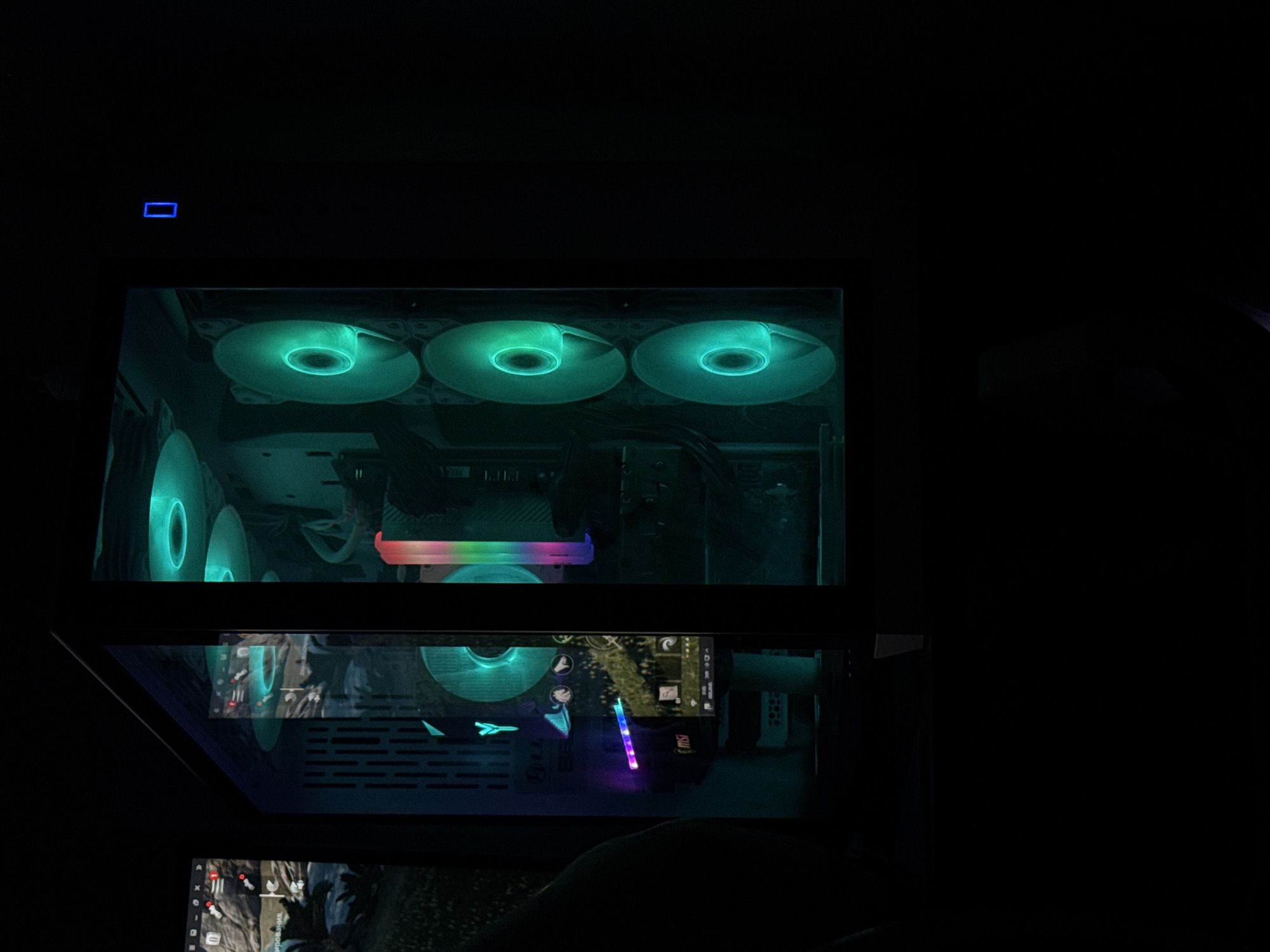 An interior shot shows a gaming PC with its side panel removed, revealing internal components lit by RGB lighting. The case is positioned in a dark room. The PC features multiple fans with green lighting, a graphics card with rainbow colored lighting, and a motherboard with blue lighting. A screen displaying a game is visible to the left, and a blue LED light is present on the right side of the case.