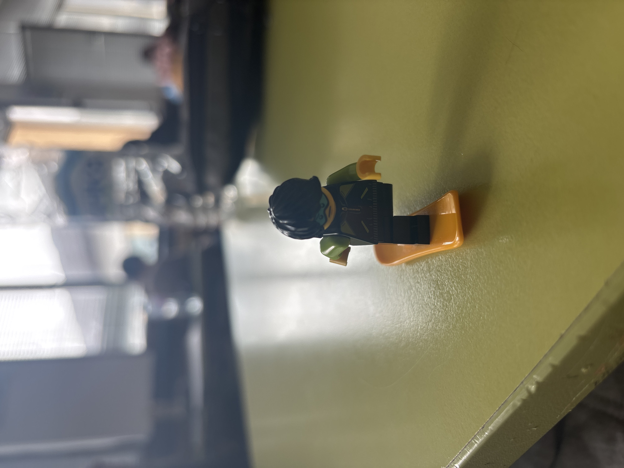 A Lego mini-figure is laying on its side on a light green surface. The mini-figure is wearing a black wetsuit, flippers, and head covering. The surroundings are blurry and indiscernible. There is no indication of the location being Zlatograd, Bulgaria.