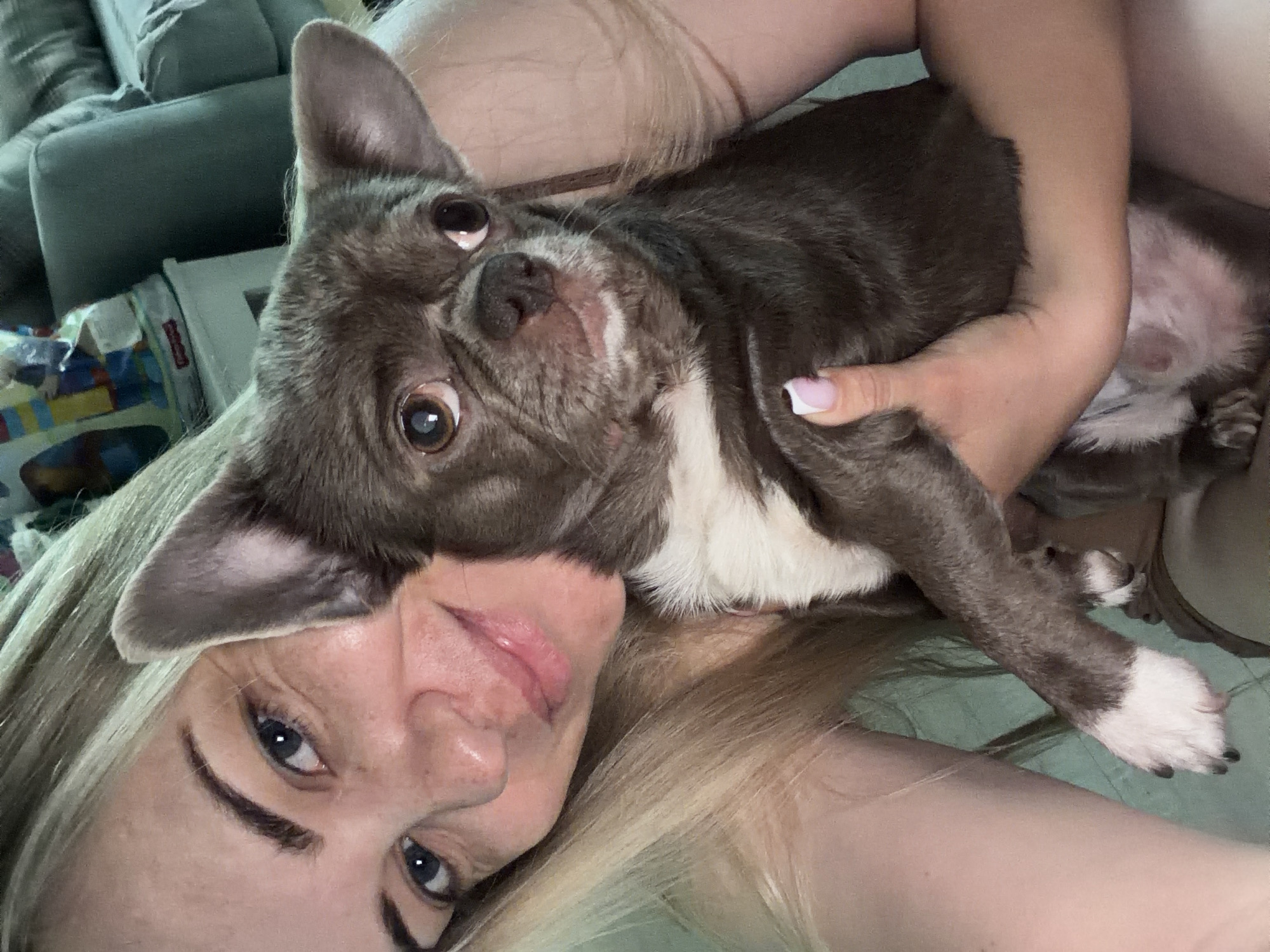 A woman with blonde hair and blue eyes is lying down, holding a small, brown and white dog. The dog is looking directly at the camera. The location is unknown, and there is no indication that it is in Votkinsk, Russia.