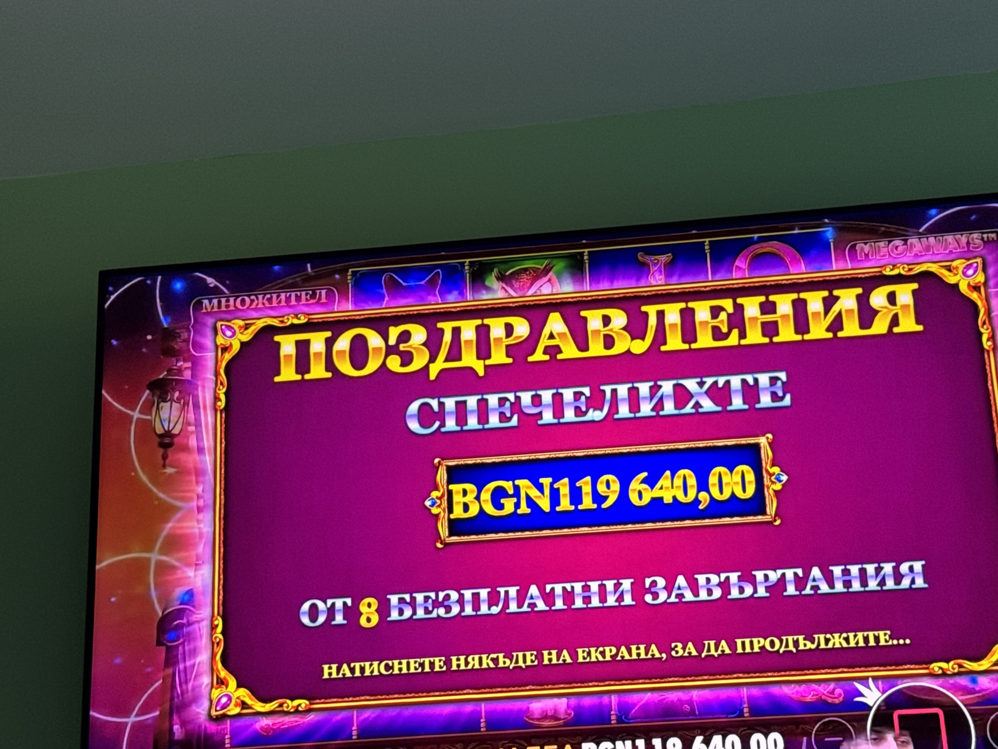 The image shows a television screen displaying a congratulations message from a slot machine game. The game has a "Megaways" feature and the player has won 119,640.00 BGN (Bulgarian Leva). The message also states the player has received 8 free spins and instructs the player to touch the screen to continue.