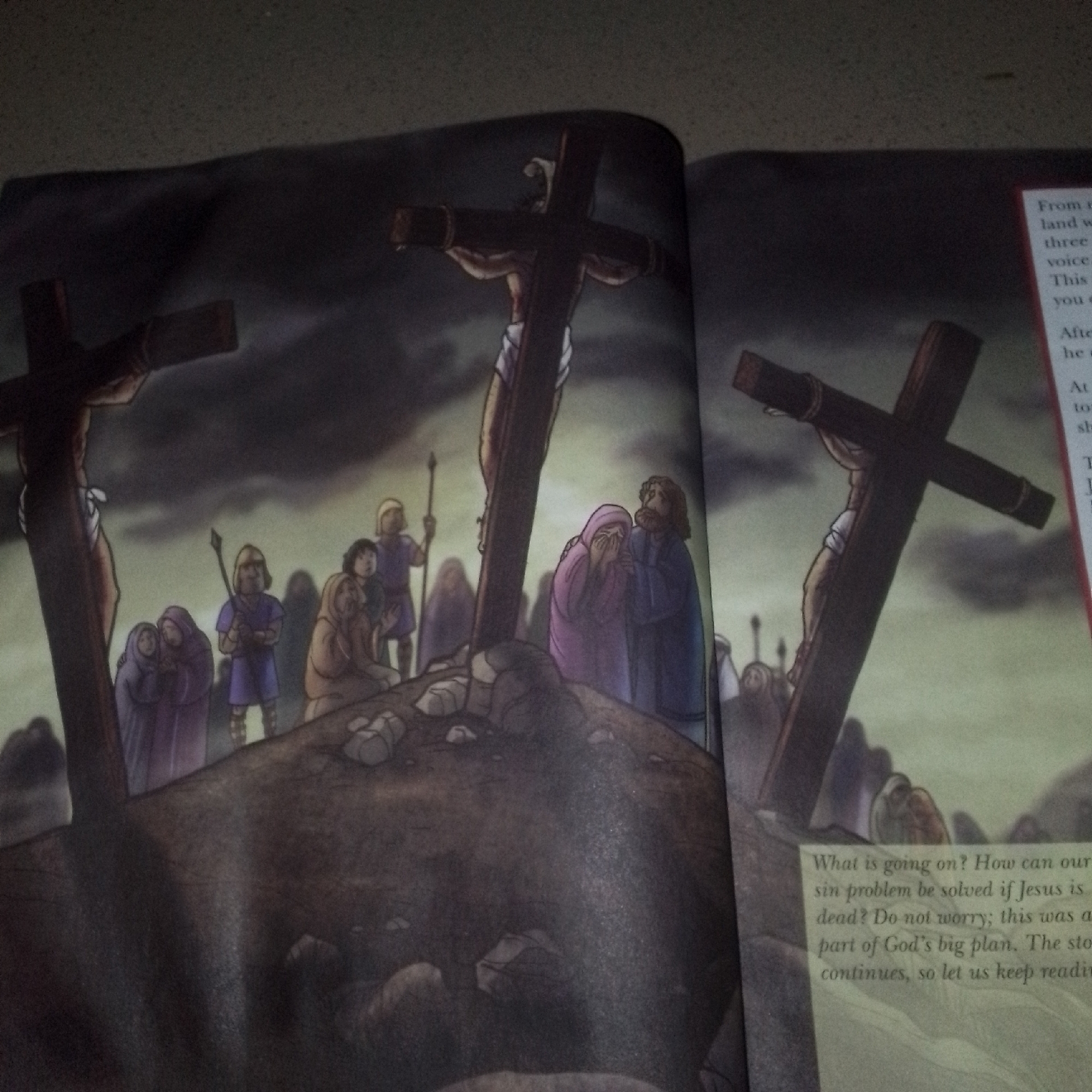 The image displays an illustration depicting the crucifixion of Jesus Christ. Two crosses are prominently featured. On the left, Jesus is shown on a cross, with a figure in white cloth around his waist. Several people in traditional attire are gathered around the base of this cross, some appearing to be mourning. To the right, another cross with a crucified figure is visible, also with onlookers. The background is dark and cloudy, suggesting a somber atmosphere. A text box in the bottom right corner contains written words, which appear to be part of a narrative related to the illustration. The overall scene suggests a biblical or religious context.