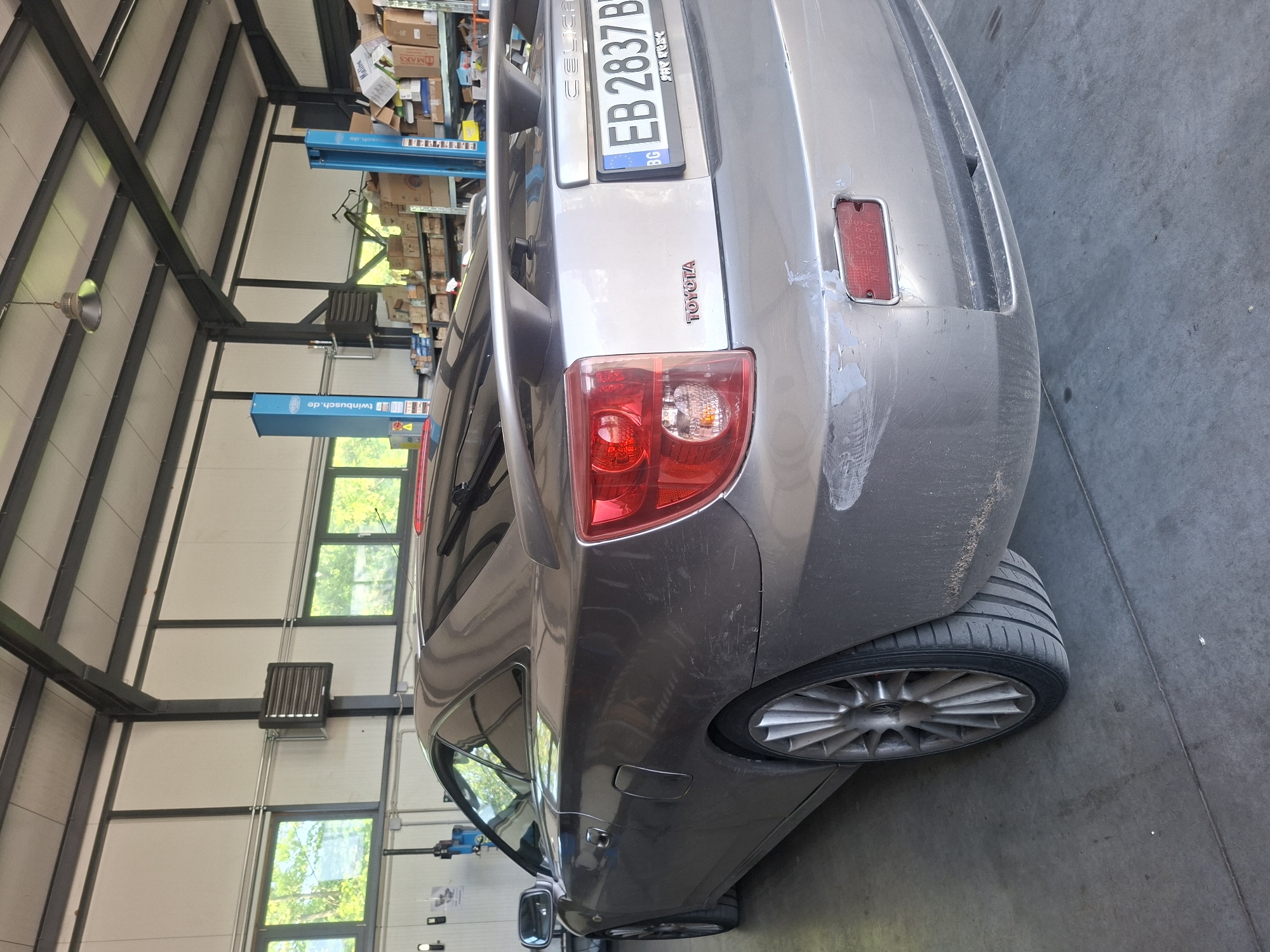 The image shows the rear of a silver Toyota Celica. The car has a Bulgarian license plate EB 2837 BP. The scene appears to be inside a garage. There are car lifts and shelves visible in the background. The city and state of the location are unknown.