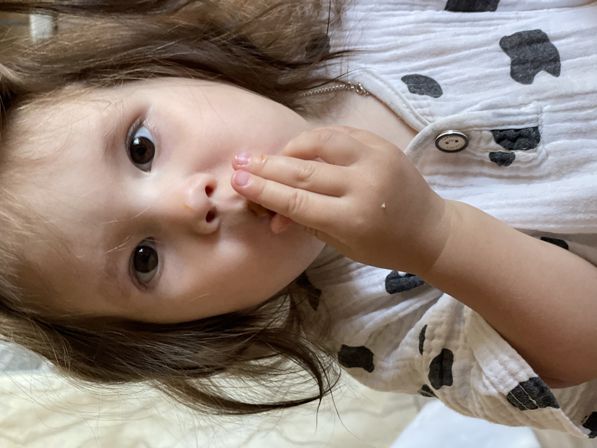 A young child with brown hair and eyes is looking directly at the camera, with their hand near their mouth. They are wearing a white shirt with a black cow print design. The location is not specified, and there is no information to suggest it is in Izhevsk, Russia.