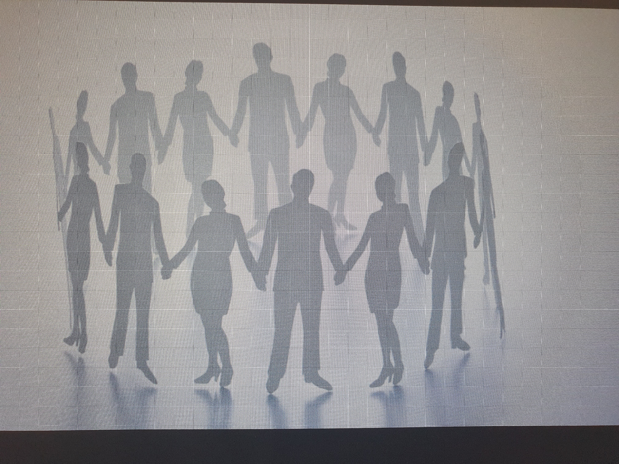 The image shows the shadows of twelve people holding hands in a semi-circle, projected onto a light-colored, textured surface. The shadows suggest a group of individuals, some appearing taller than others, forming a cohesive unit. The scene is abstract and lacks specific environmental details, making it impossible to determine the location within Tashkent, Uzbekistan. The focus is on the silhouettes and the symbolic representation of unity or connection.