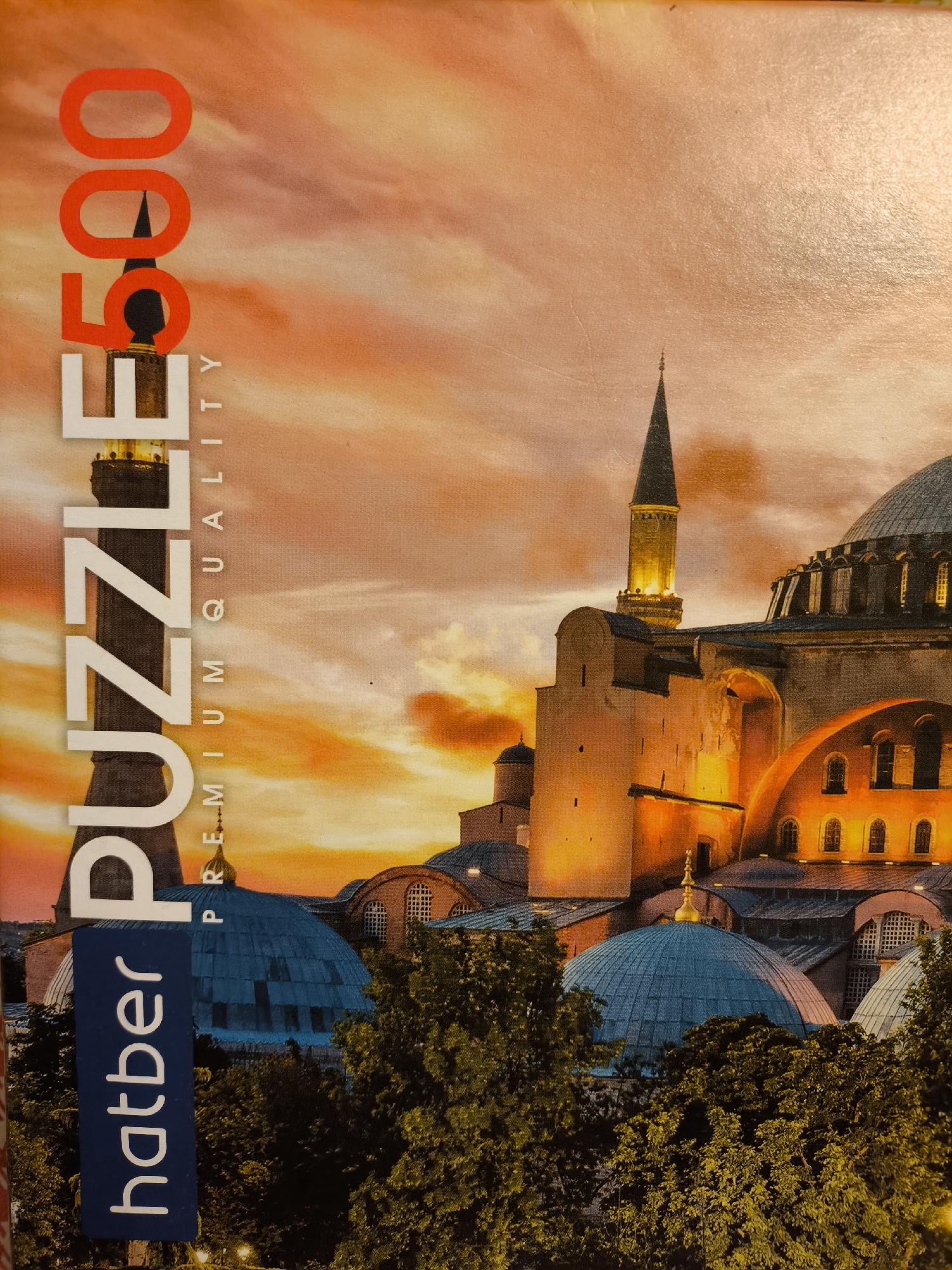 The image depicts a 500-piece puzzle box. The artwork on the box features a building with a distinctive minaret and a large dome, likely the Hagia Sophia in Istanbul, Turkey, at sunset. The text "PUZZLE 500" is vertically oriented on the left, and the brand name "hatber" is in a blue rectangle below "PUZZLE". The text "PREMIUM QUALITY" is displayed vertically in smaller font between "PUZZLE" and "500". The background consists of an orange sky behind the building and trees in the foreground. The image is not in the city of Khimki, Russia; it is located in Istanbul, Turkey.