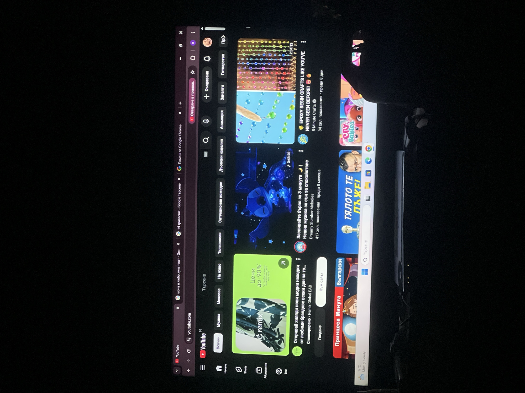 The image shows a tablet screen displaying the YouTube homepage in Bulgarian. The page features various videos and channels, including content related to music, comedy, crafts, and children's shows. The interface includes standard YouTube navigation elements such as the search bar, channel icons, and category selections. The date and time are not visible. There are no people or specific subjects in the image other than what is displayed on the screen. The image was taken at night, as evidenced by the dark background. There is no explicit connection to the city of Cherven Bryag, Bulgaria other than the language setting of the interface, which may indicate a user location.
