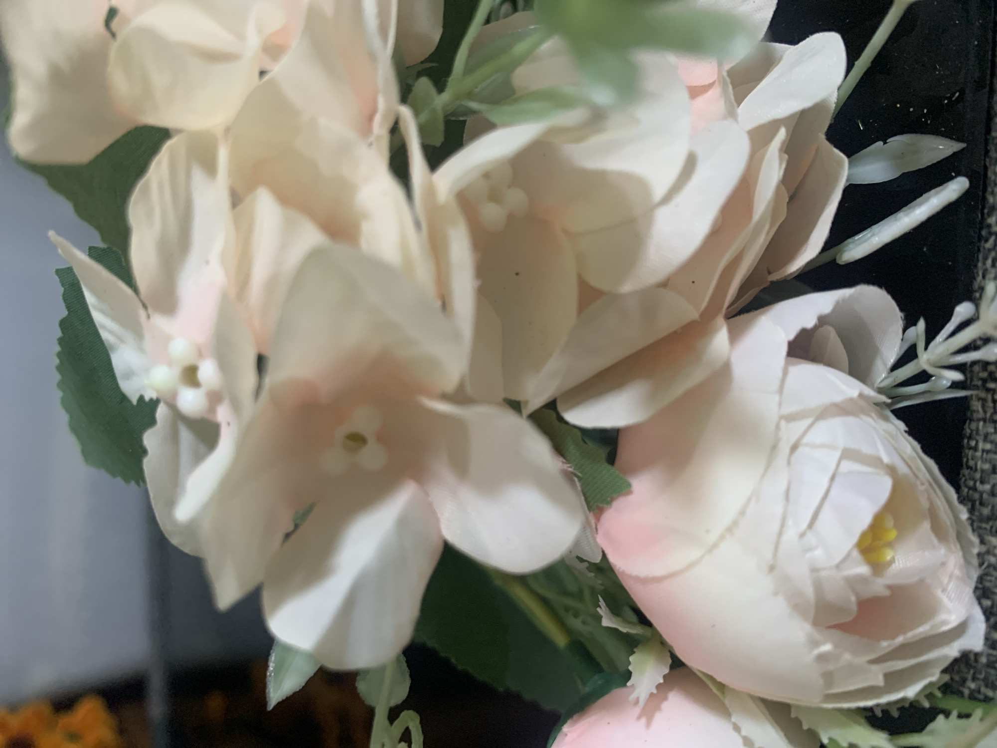 The image shows a close-up view of artificial flowers with light pink and white petals. The flowers are arranged in a bouquet, with some green leaves and stems visible. The background is dark and out of focus, making it difficult to discern any specific environmental details. The lighting is soft, highlighting the delicate texture of the petals. There are no people or actions depicted in the image. The location in Kuala Pembuang, Indonesia, is not discernible from the visual information provided in the image.